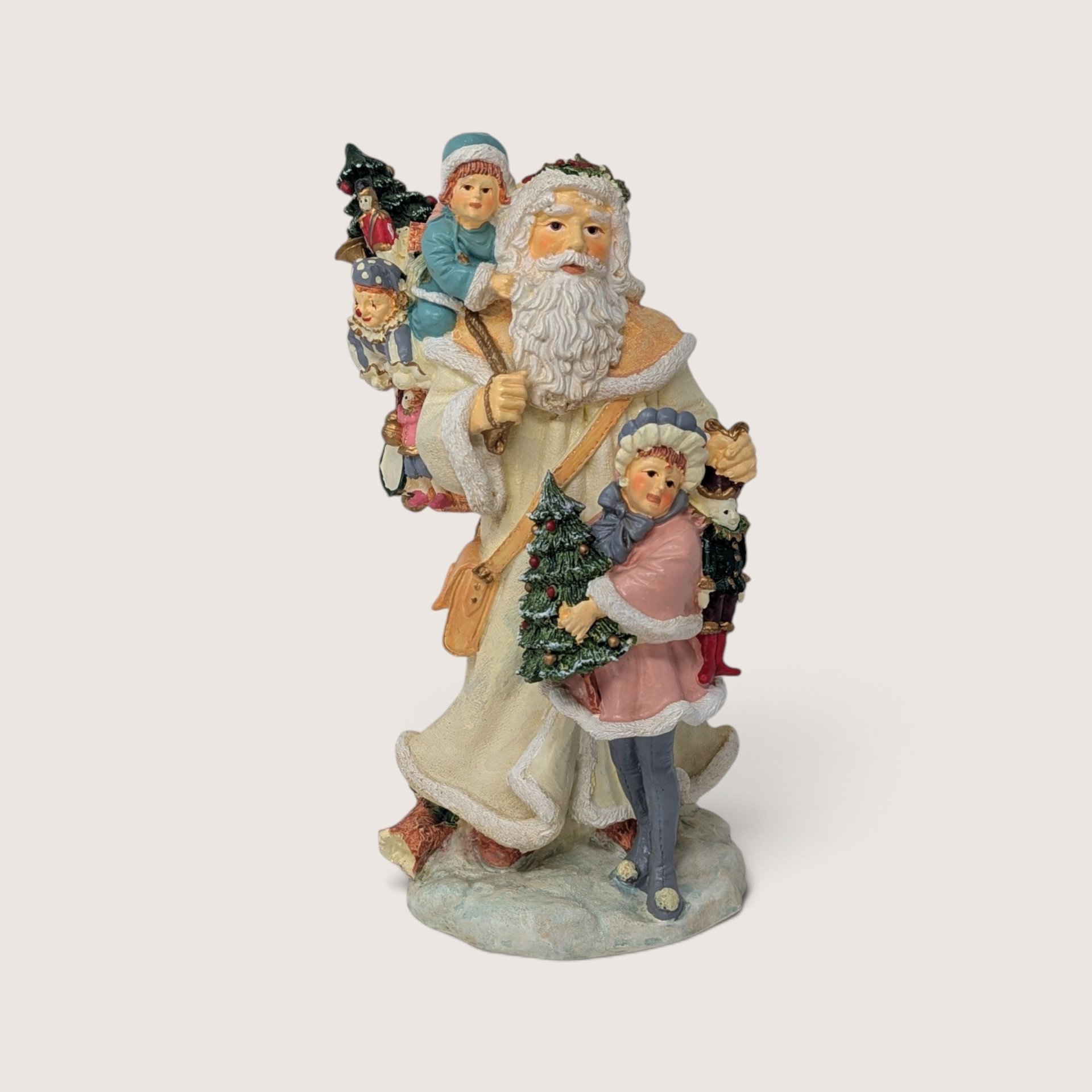 Vintage holiday figurine of Santa Claus in a cream coat holding a small tree with children and toys.