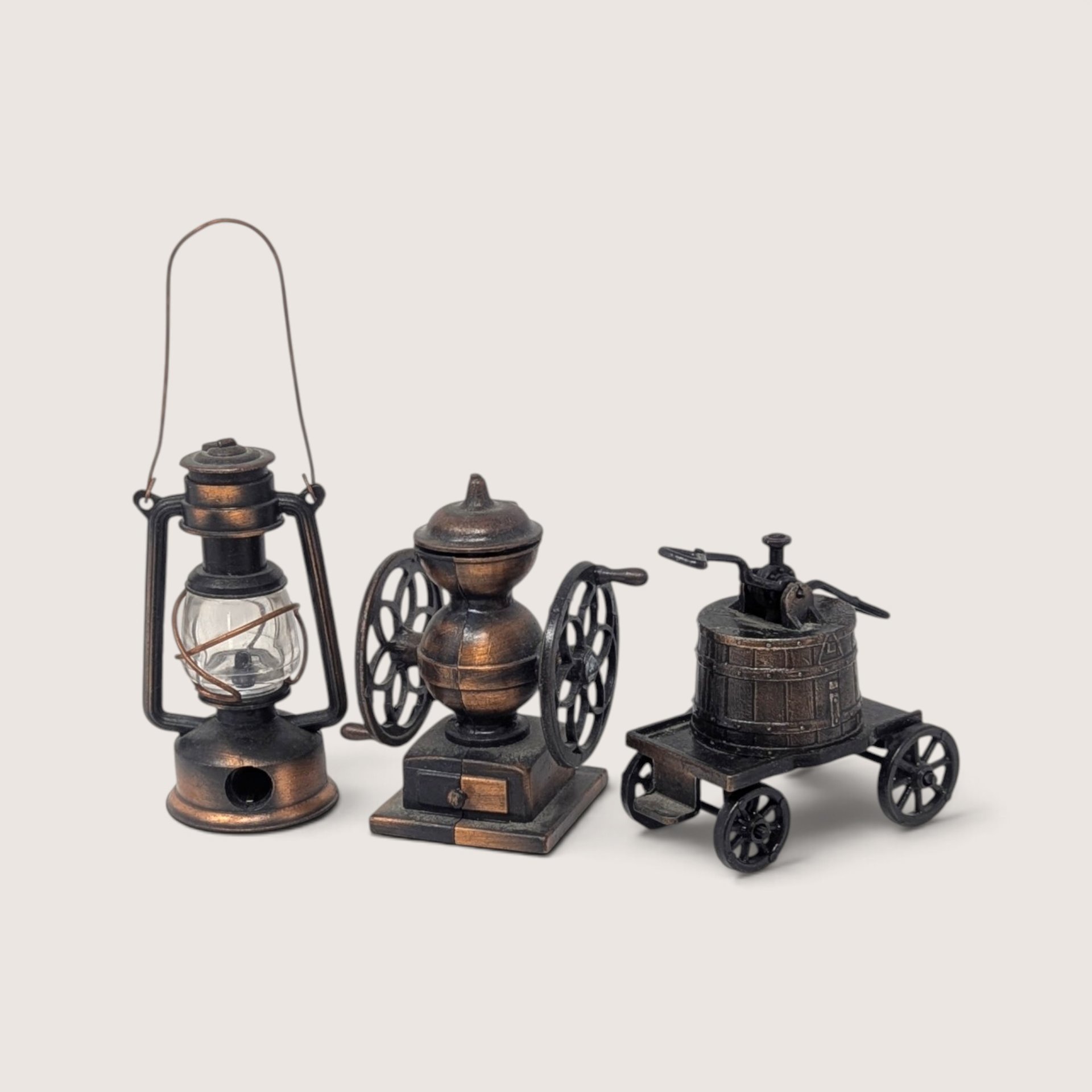 Set of three vintage miniature metal and plastic pencil sharpeners shaped like a lantern, coffee grinder, and wheeled cart.