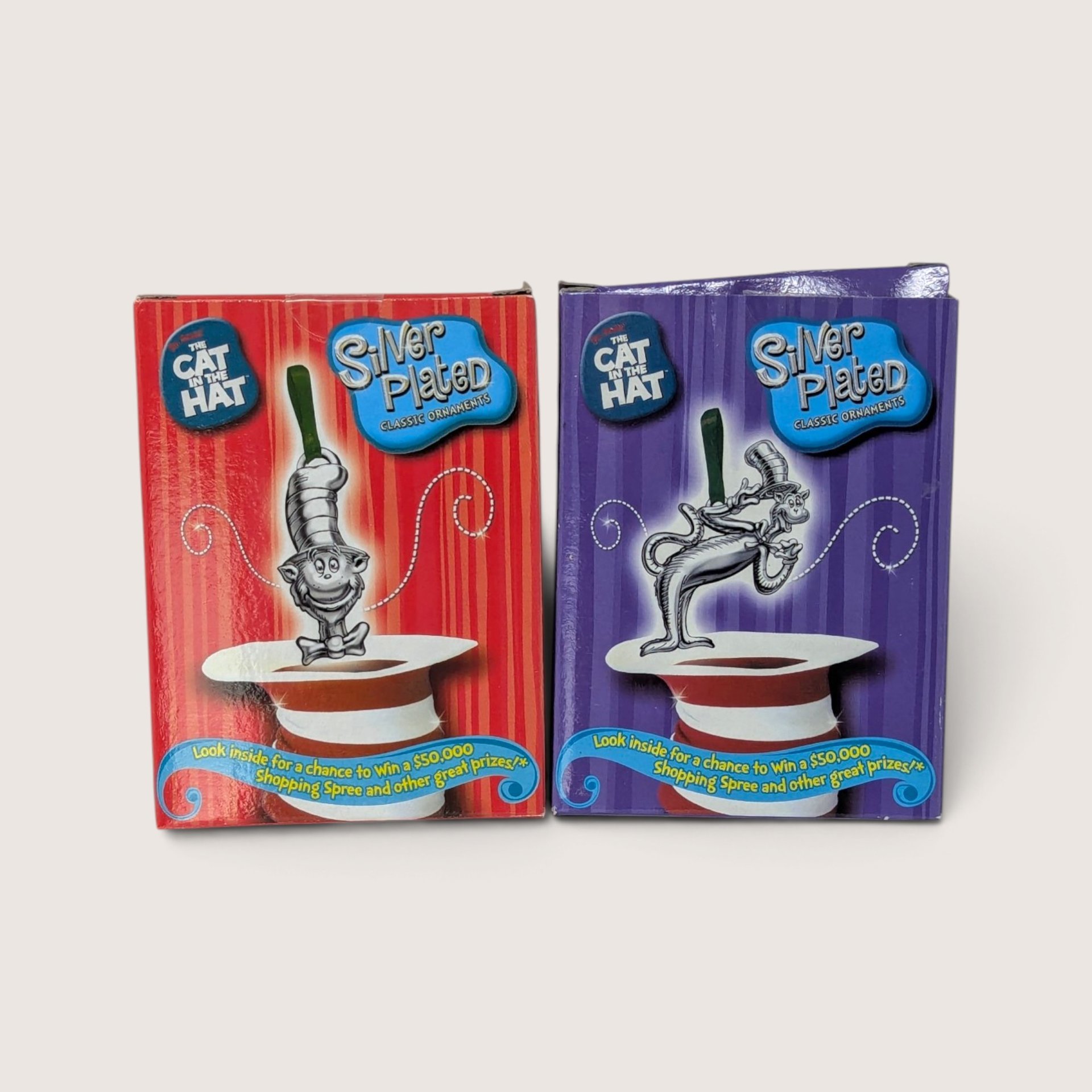 A pair of vintage Cat in the Hat silver-plated classic ornaments shown in their red and purple original boxes against a neutral background.