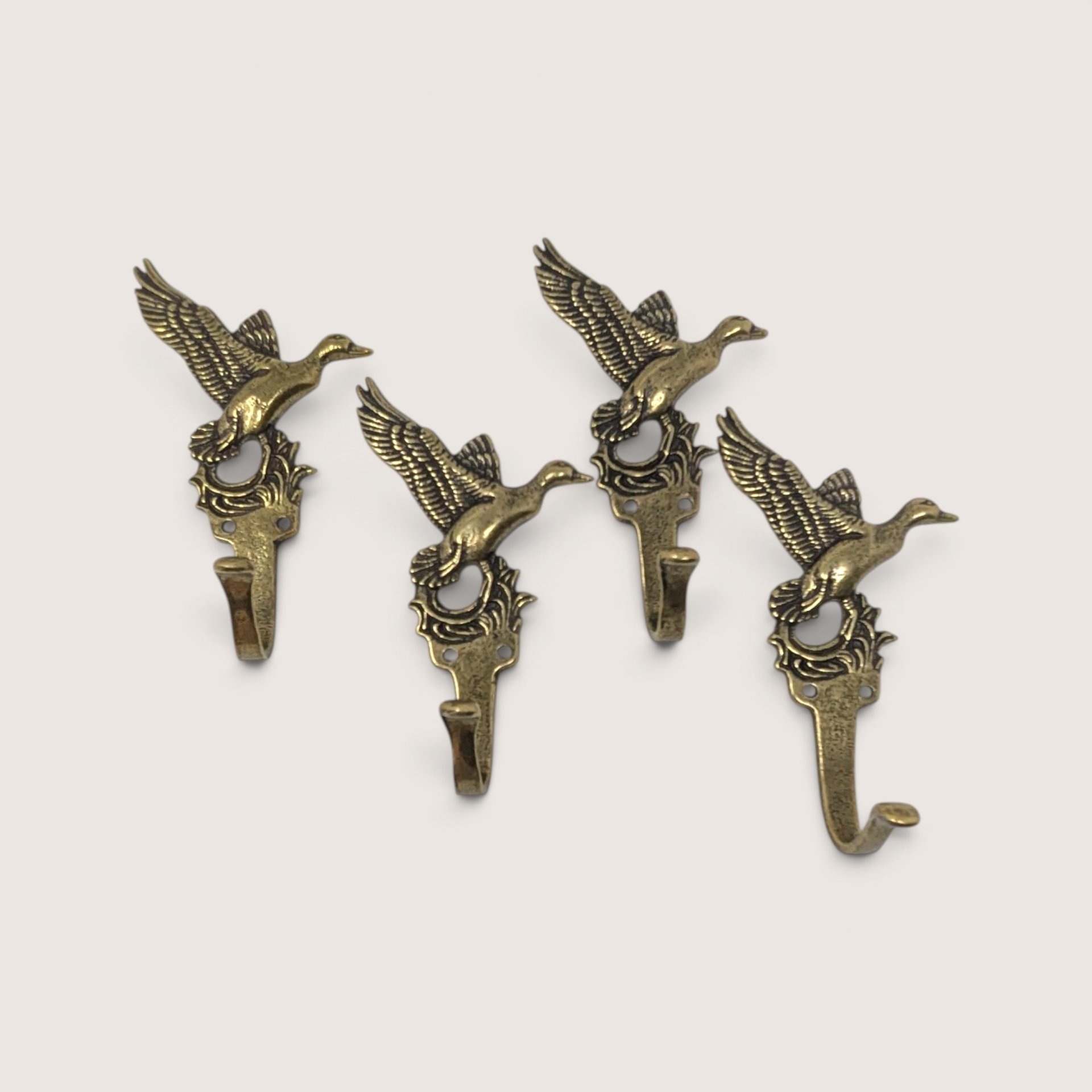 A set of four vintage metal wall hooks shaped like flying ducks with an antique brass finish arranged against a neutral background.