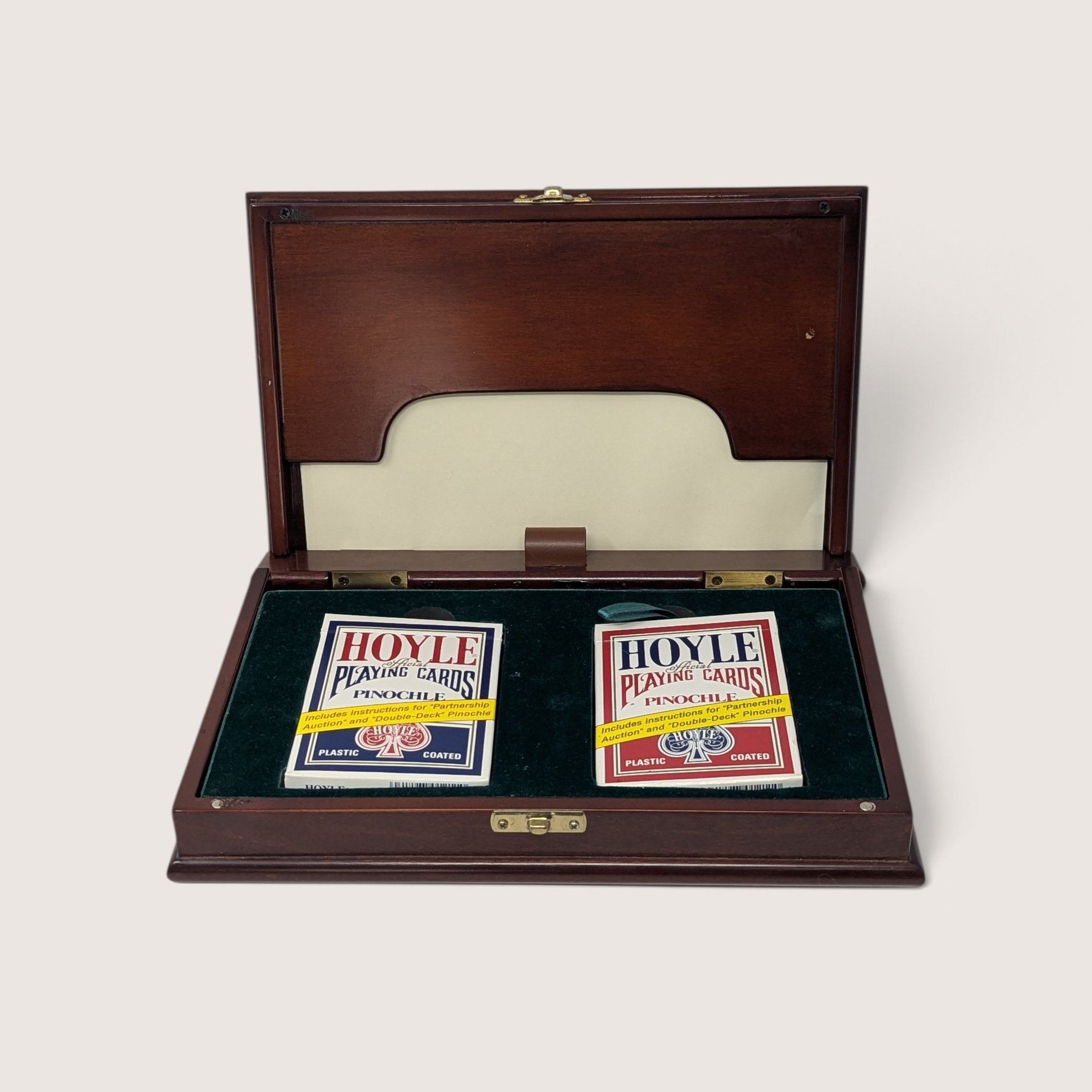 An open vintage wooden pinochle card box lined with green felt and holding two decks of Hoyle pinochle playing cards against a neutral background.
