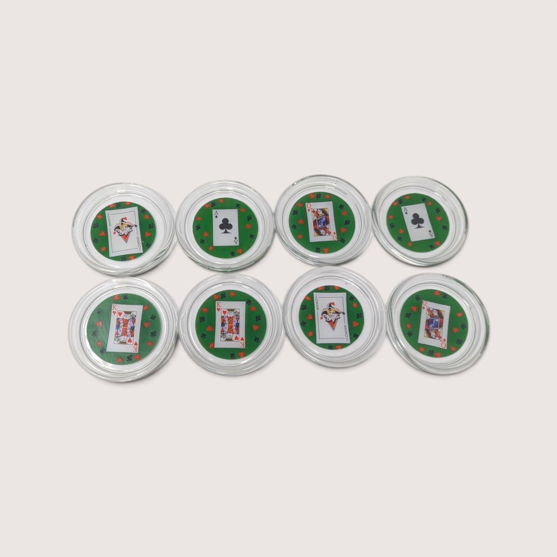 A set of 8 round glass coasters featuring miniature playing card inserts including jokers, kings, queens, and aces against a green background.