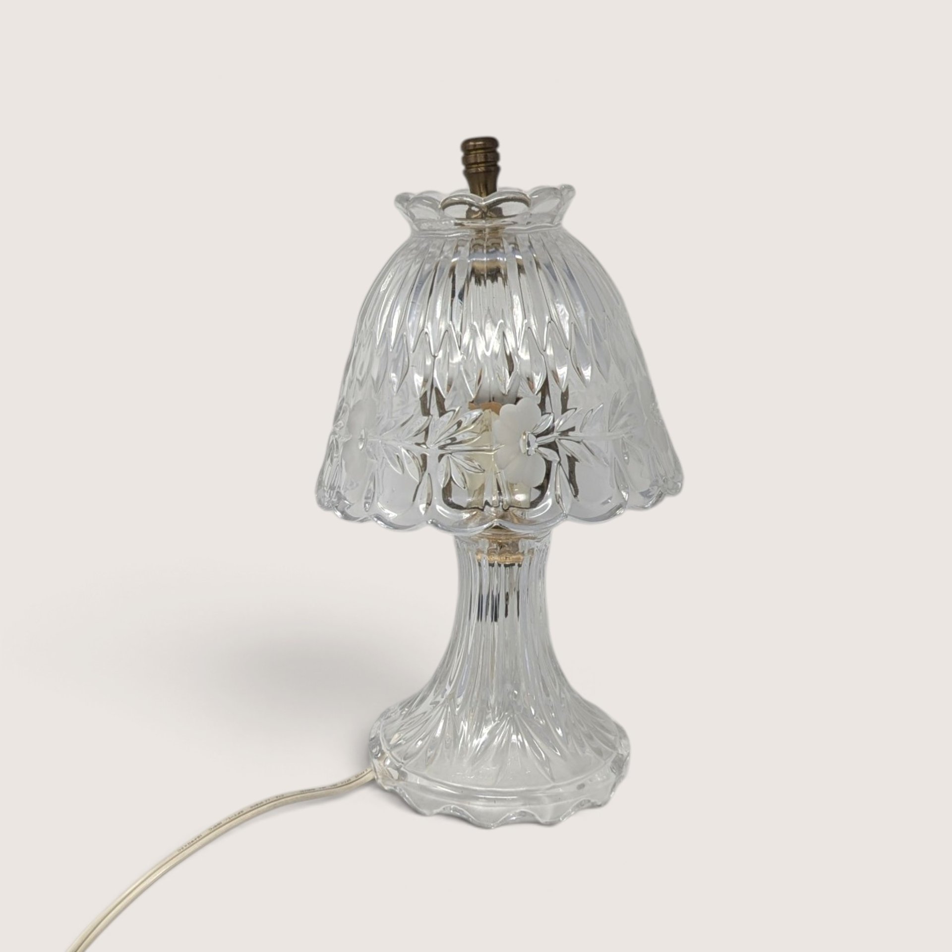 A small vintage clear cut glass boudoir lamp featuring a patterned shade with frosted floral details and a fluted base against a neutral background.