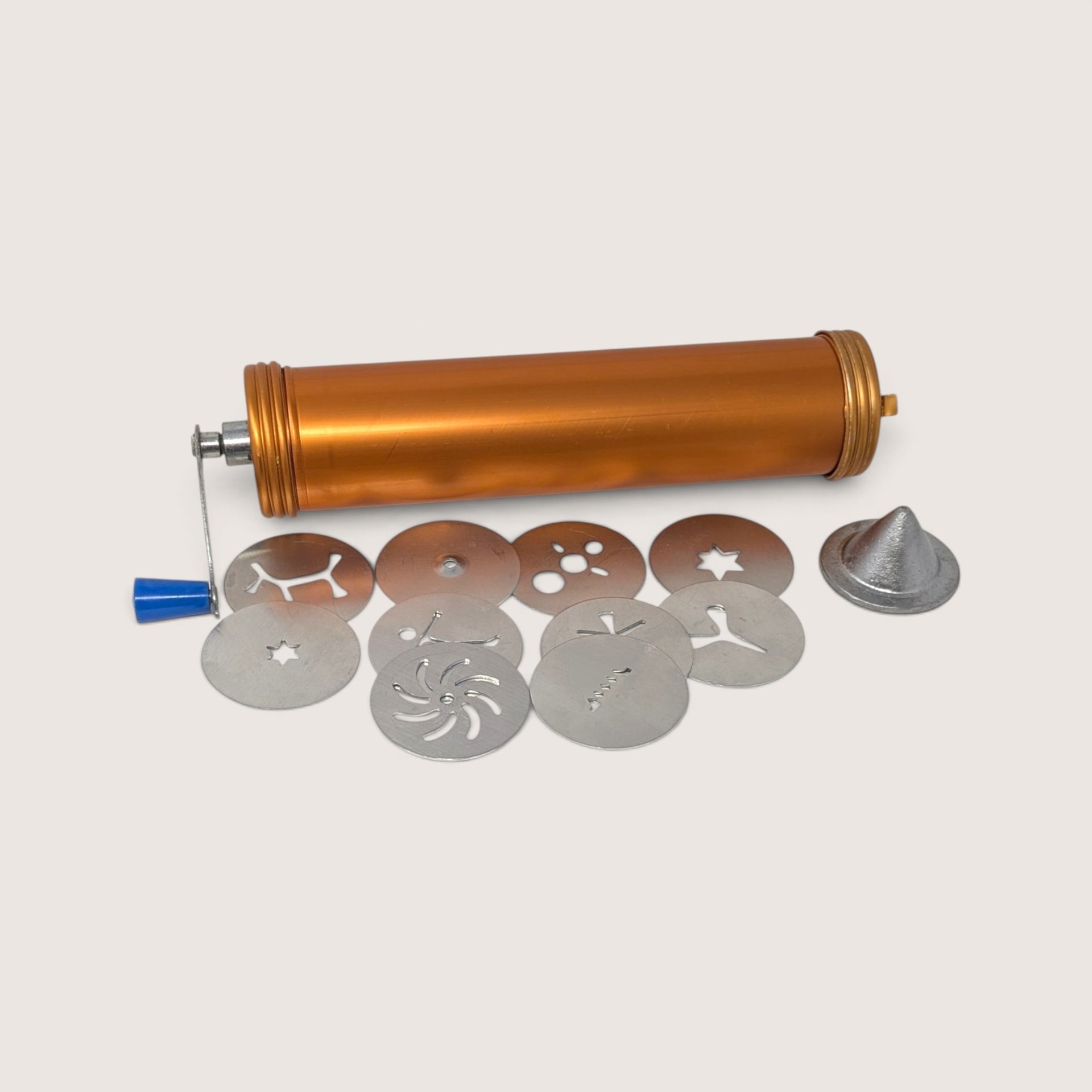 A vintage copper-colored NordicWare Deluxe Cookie King cookie press cylinder displayed alongside a crank handle, various shaping discs, and a nozzle attachment against a neutral background.