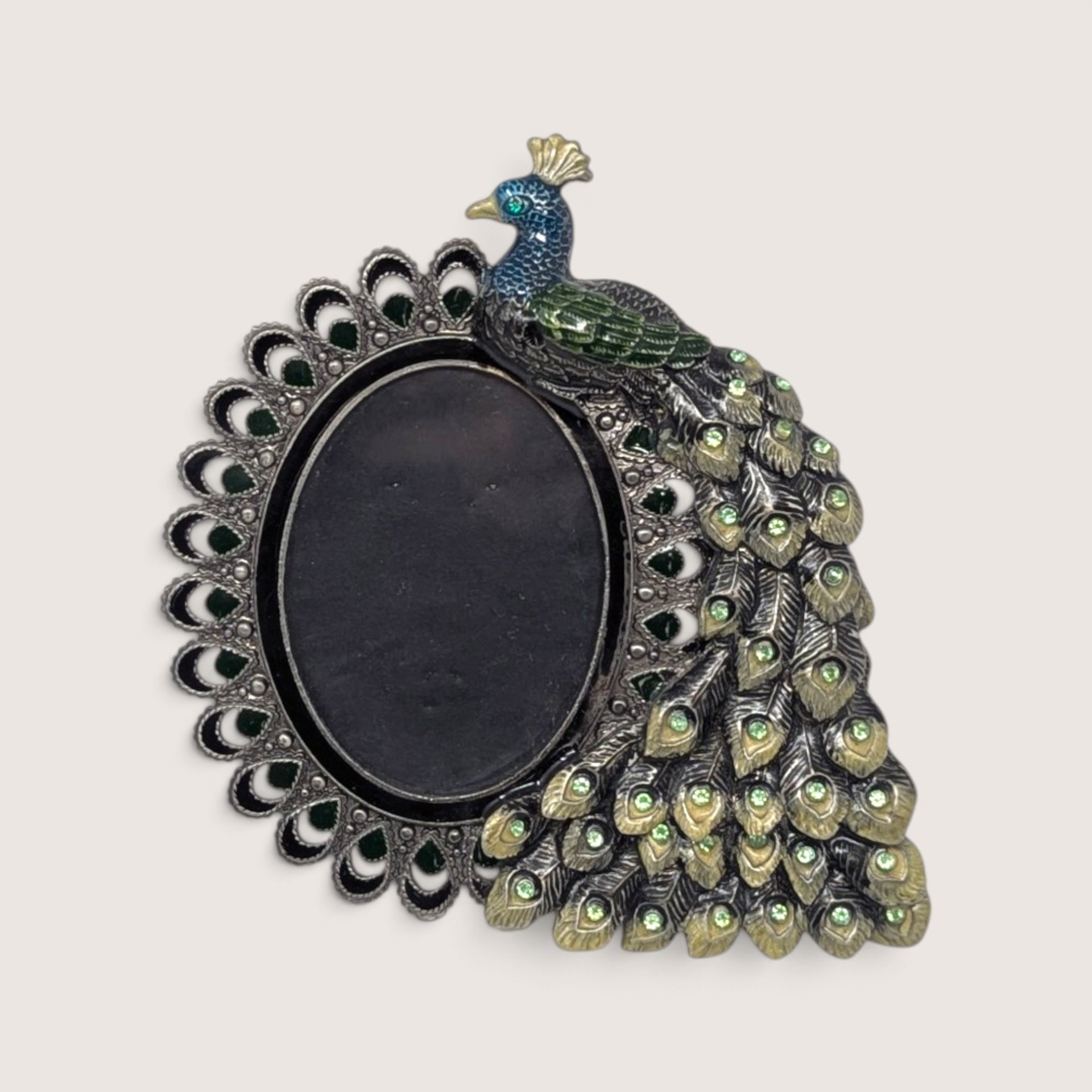 An ornate vintage metal photo frame shaped like a peacock with blue and green enamel detailing and sparkling rhinestone crystal accents surrounding an oval picture opening.
