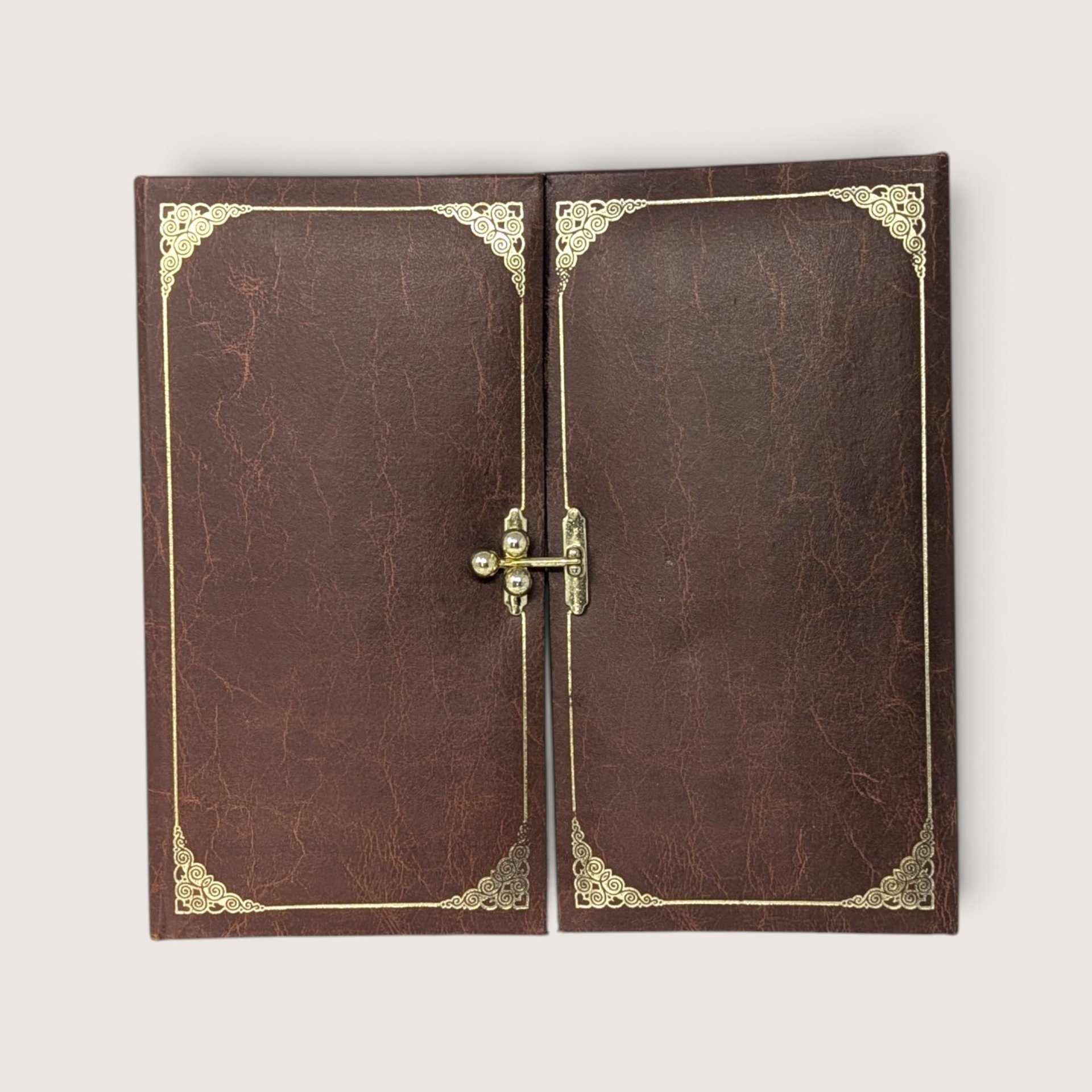 A vintage brown tri-fold photo album with gold filigree corner accents and a central gold-tone metal latch closure resting against a neutral background.