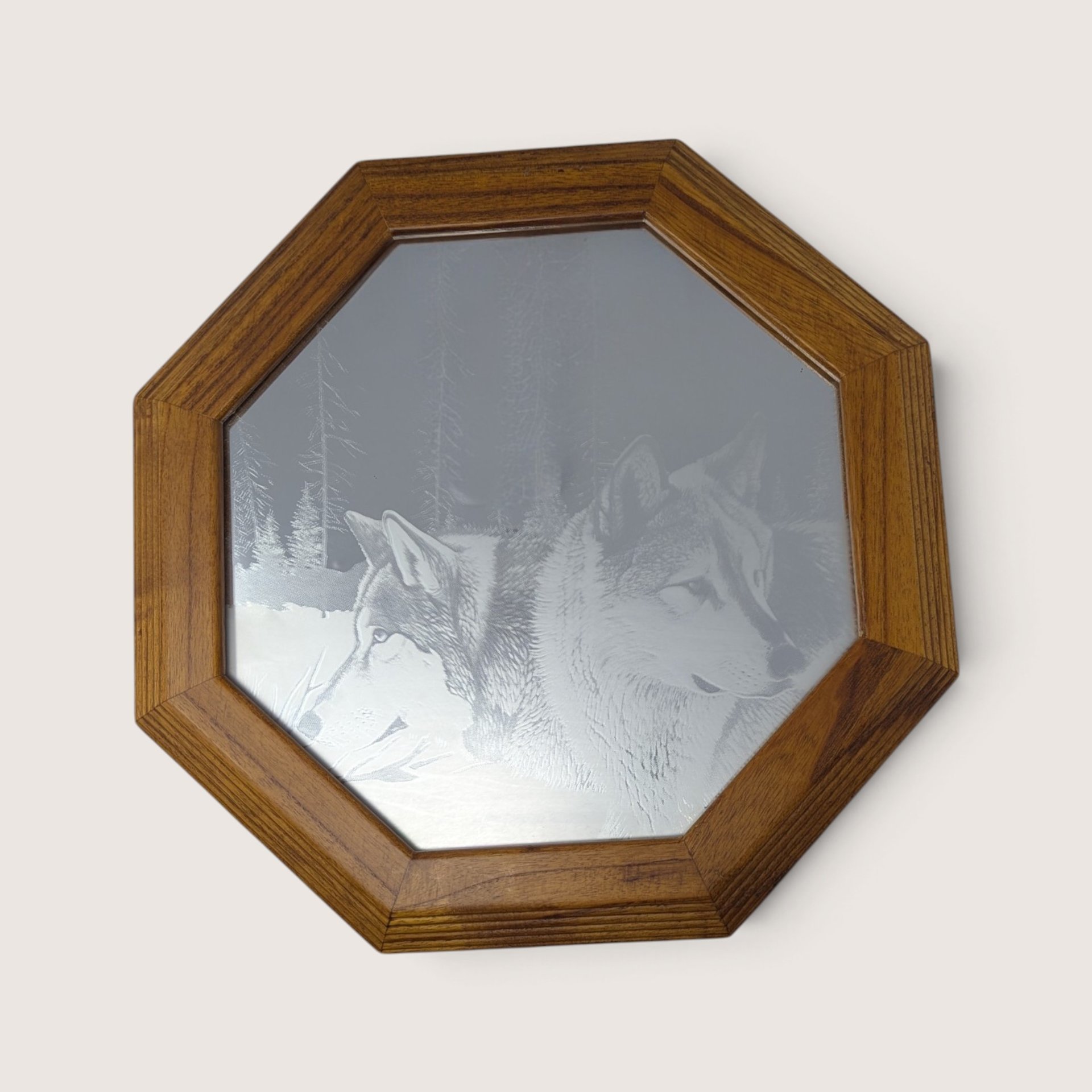 A vintage octagonal wall mirror with a wooden frame featuring an etched design of two wolves resting in a snowy pine forest.