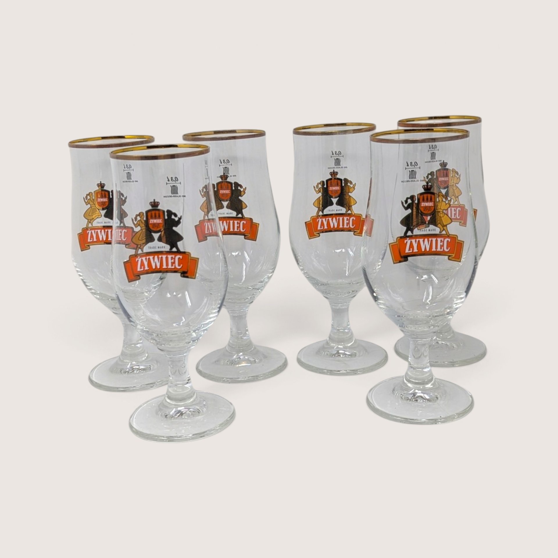 A set of six vintage Ritzenhoff Cristal Zywiec stemmed beer glasses with gold rims and folkloric graphics, displayed with their original packaging box.