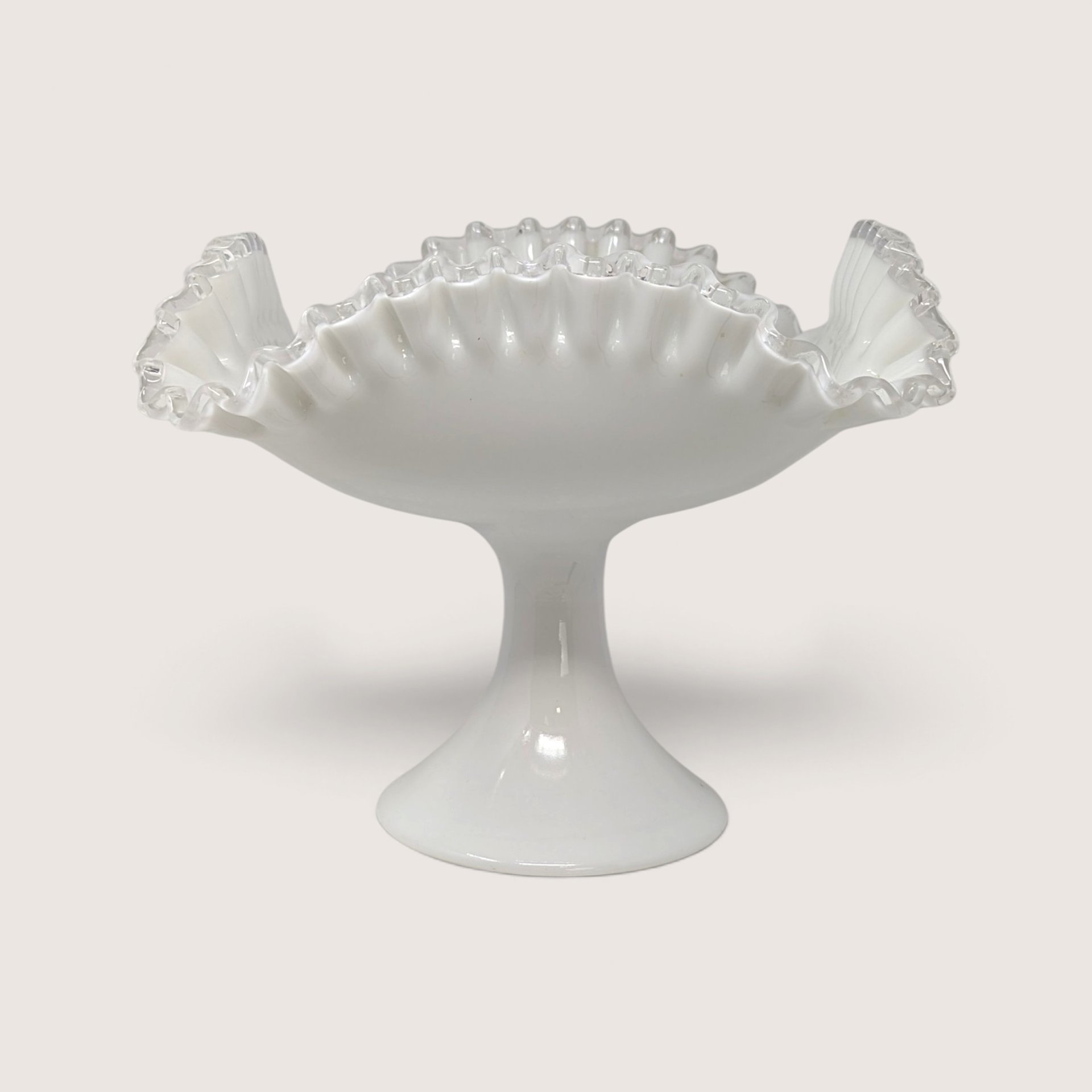 A large vintage white milk glass pedestal bowl with a dramatic swung ruffled rim and a solid footed base.