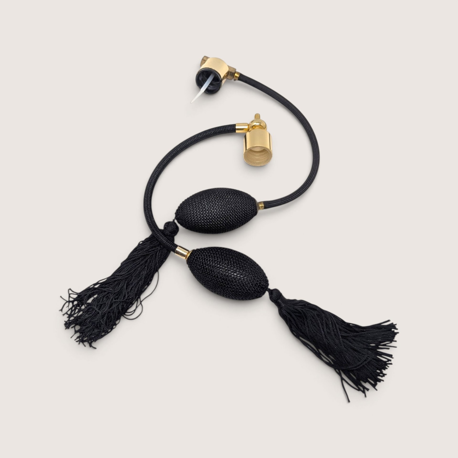 A pair of vintage black woven perfume atomizer bulbs with decorative tassels, gold-tone collars, and cords.