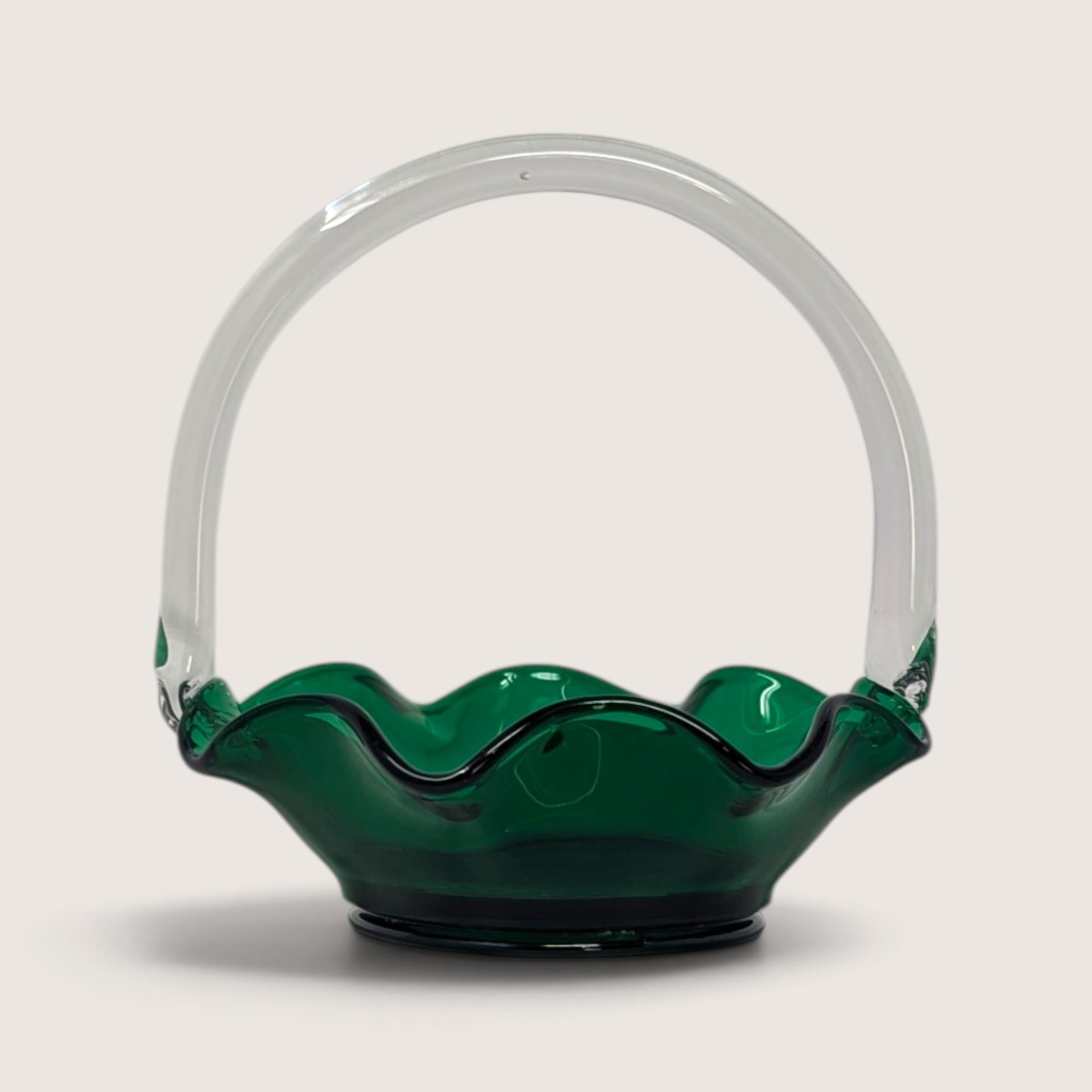 A vintage green art glass basket with a ruffled crimped rim and an applied clear glass handle.