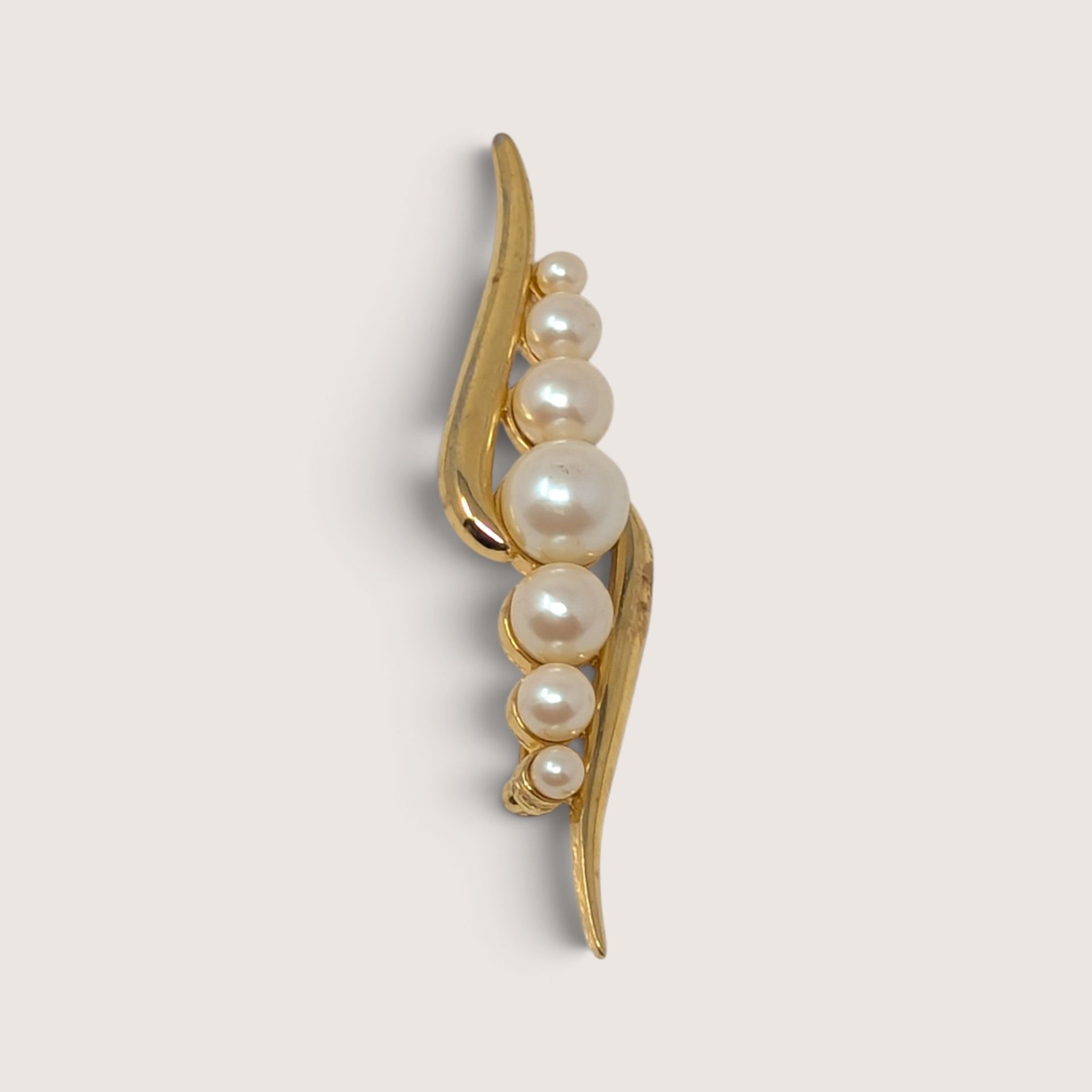 A vintage Monet gold-tone brooch shaped in a sweeping swirl motif and inset with a graduated line of creamy faux pearls.