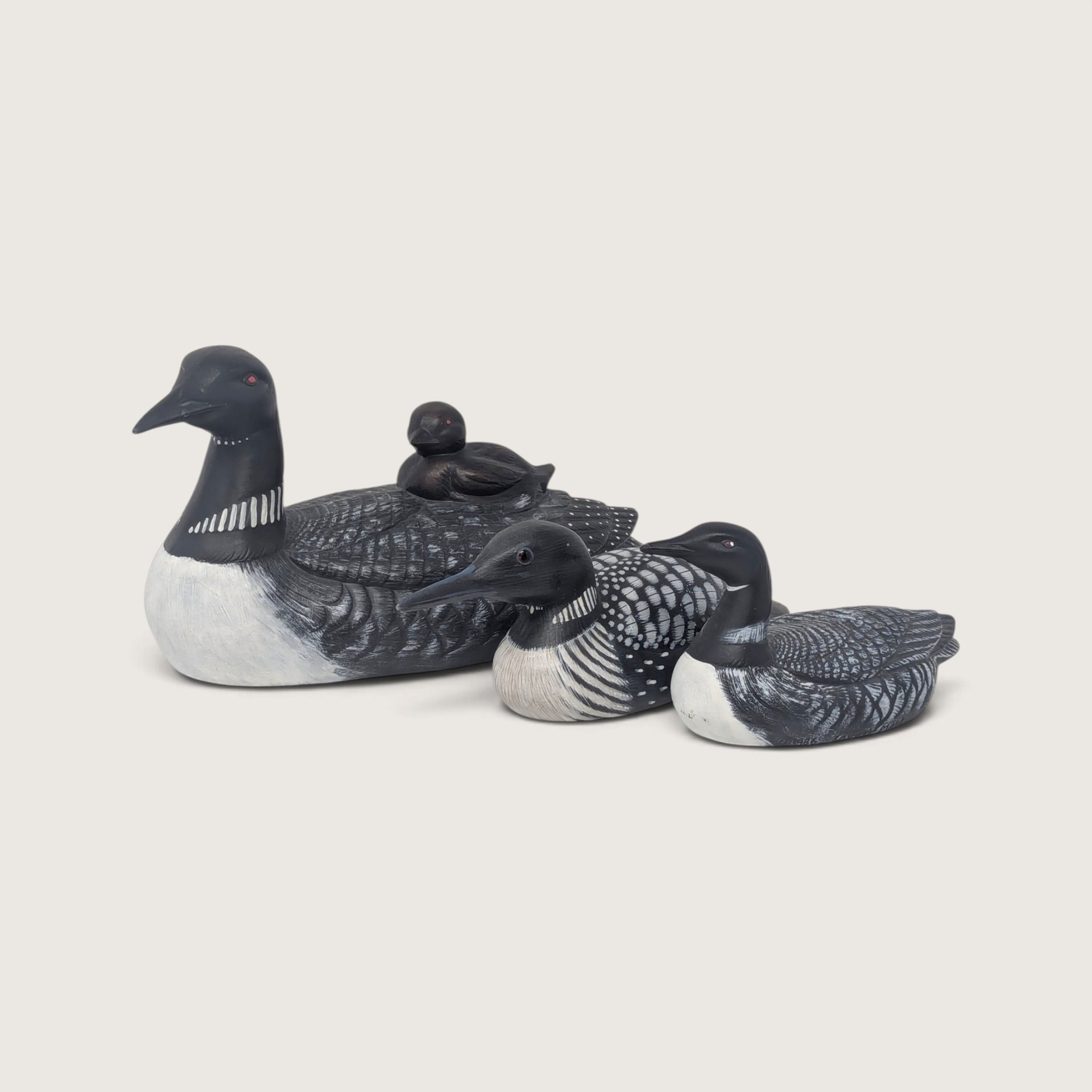 A set of three vintage hand-painted loon figurines in varying sizes, including one ceramic adult loon with a chick on its back, a wooden loon, and a smaller ceramic loon.