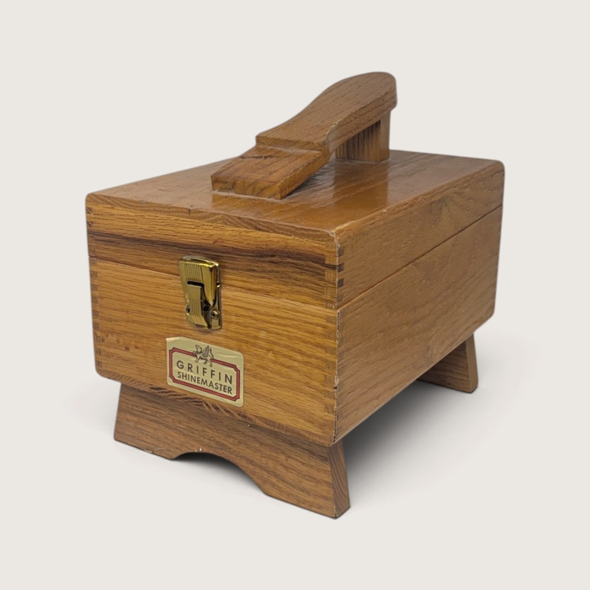 A vintage wooden Griffin Shinemaster shoe shine box with a built-in footrest on top, a brass latch, and a maker's label on the front.