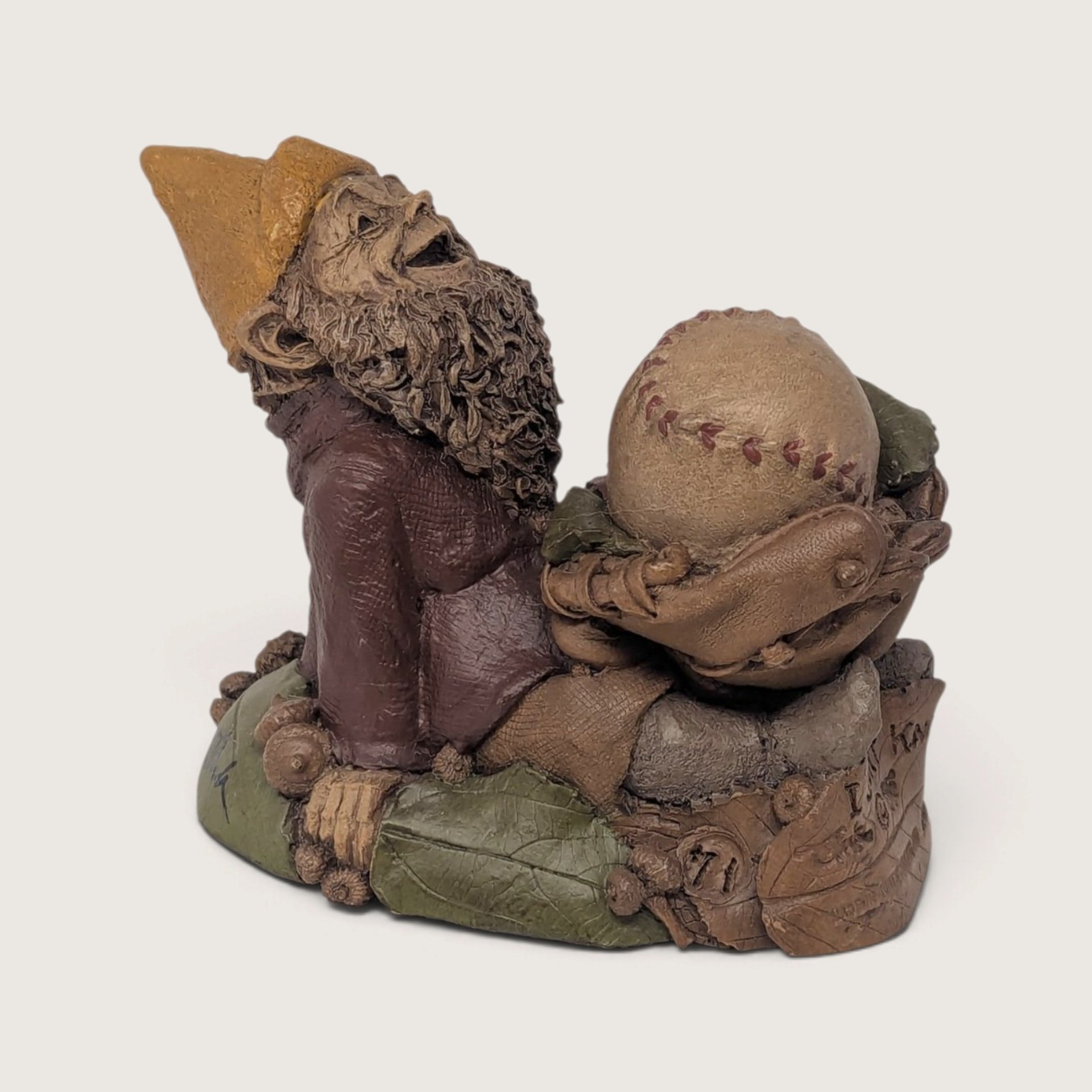 A vintage 1986 Tom Clark resin gnome figurine named I Don't Know leaning against a giant baseball on a neutral background.