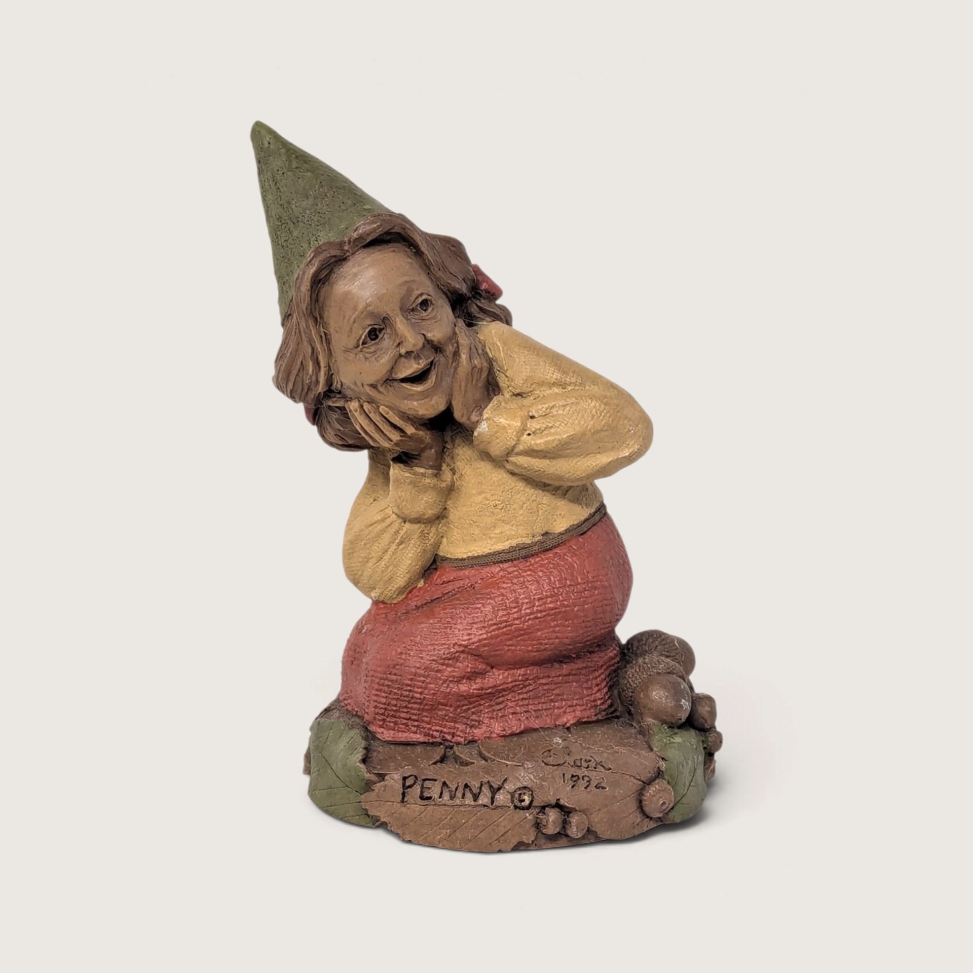 A vintage 1990s Tom Clark resin gnome figurine named Penny resting near acorns on a neutral background.