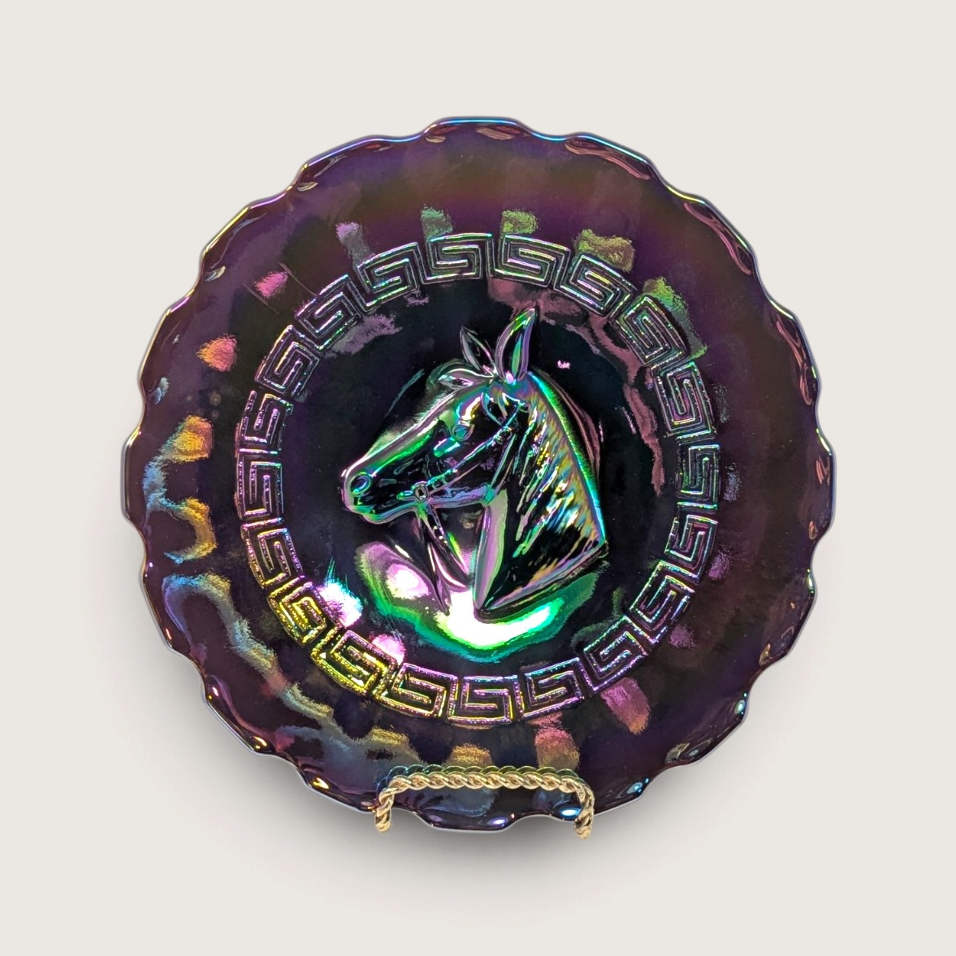 A vintage Dugan amethyst carnival glass plate featuring a central horse head and Greek key border on a neutral background.