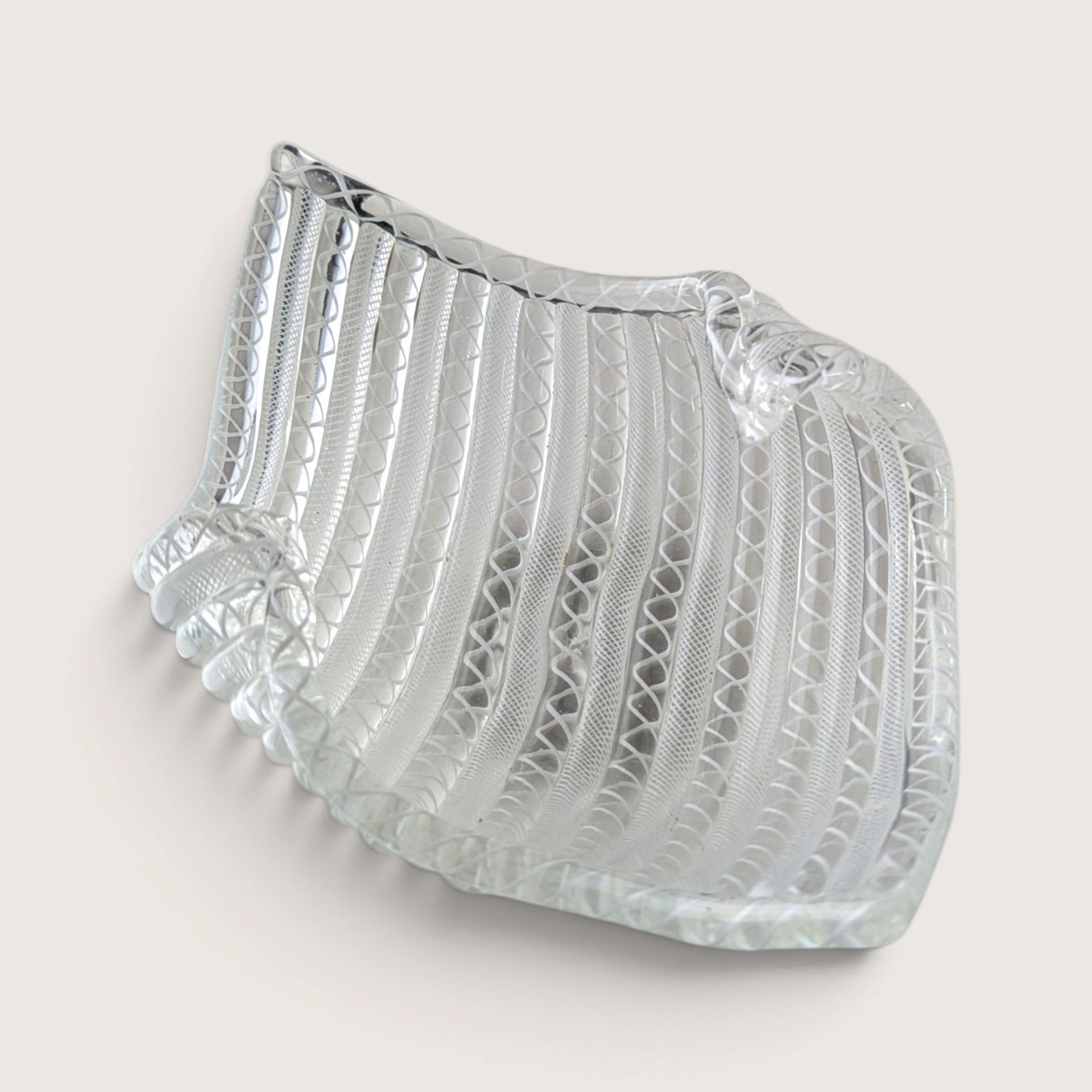 A vintage clear and white latticino optic ribbed art glass folded bowl with a handkerchief rim on a neutral background.