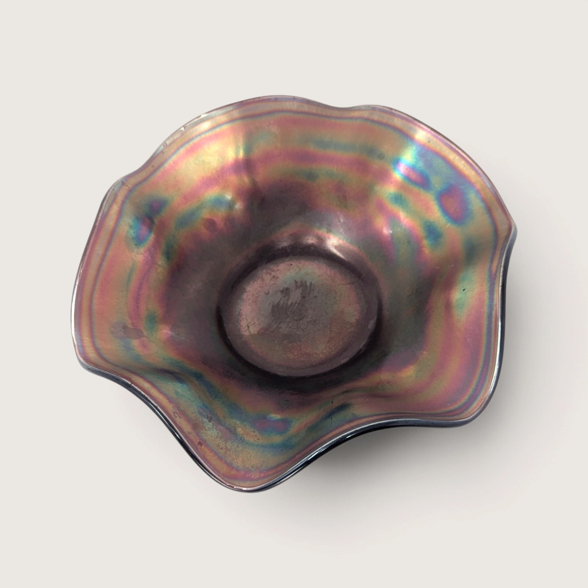 1910s Northwood amethyst carnival glass ruffled bowl showing a floral exterior pattern and an underlined n mark on a neutral background.