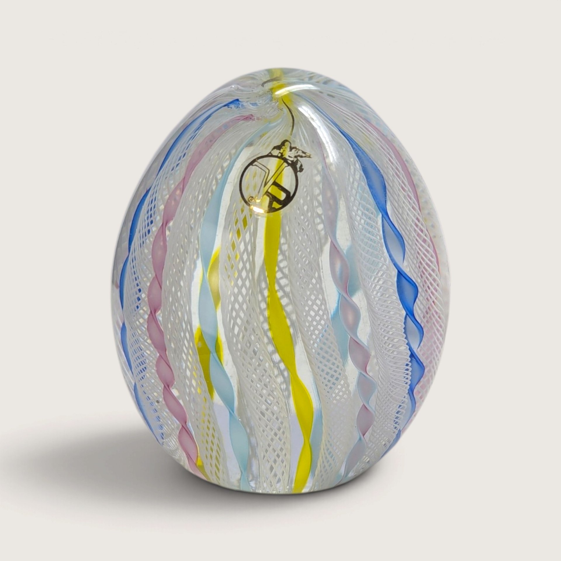 A vintage Vecchia Murano hand-blown glass paperweight egg featuring vertical white latticino lace and colorful twist ribbons with a VR sticker on a neutral background.   