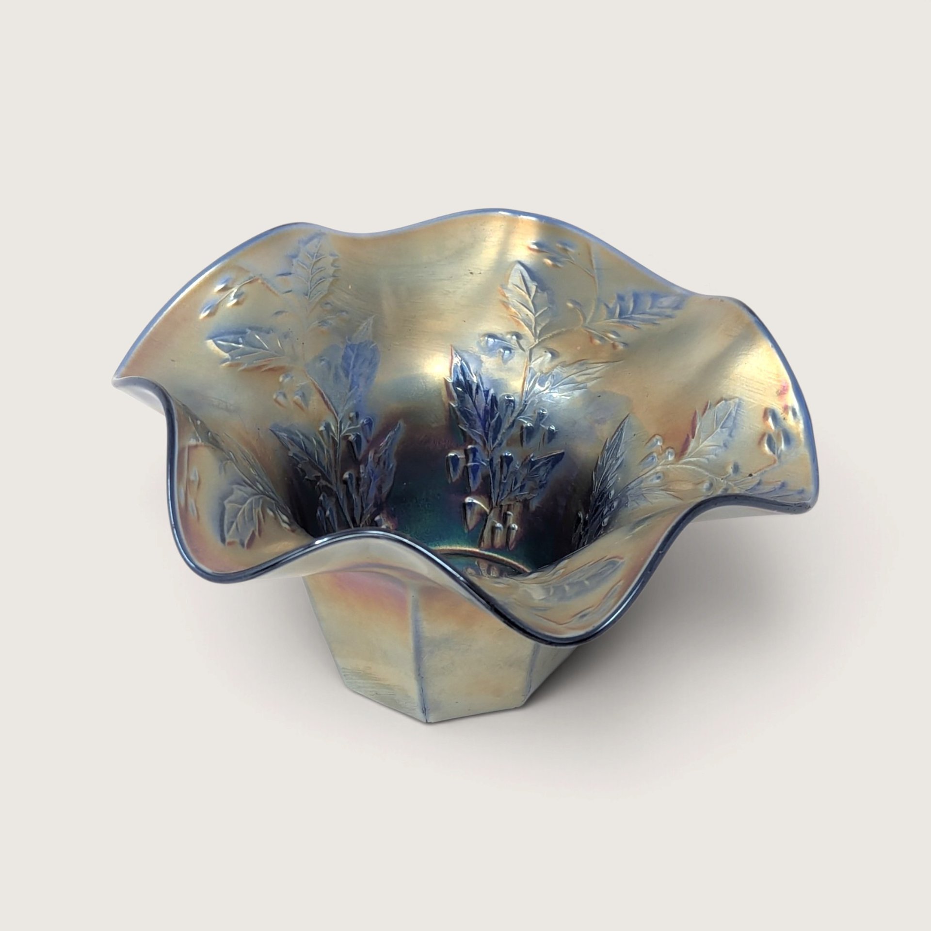 A vintage Fenton blue carnival glass fluted vase featuring an embossed holly pattern and a ruffled edge on a neutral background.