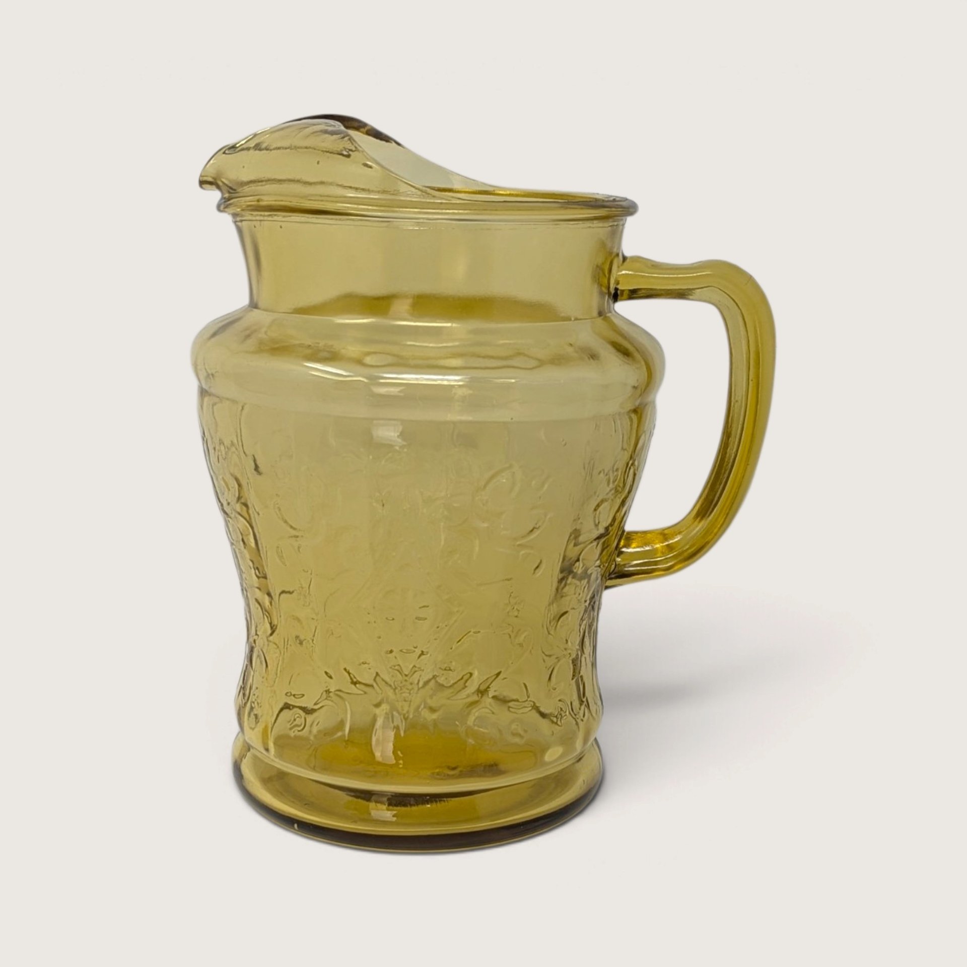 A vintage Federal Glass amber yellow depression glass pitcher featuring the Madrid scroll pattern on a neutral background.