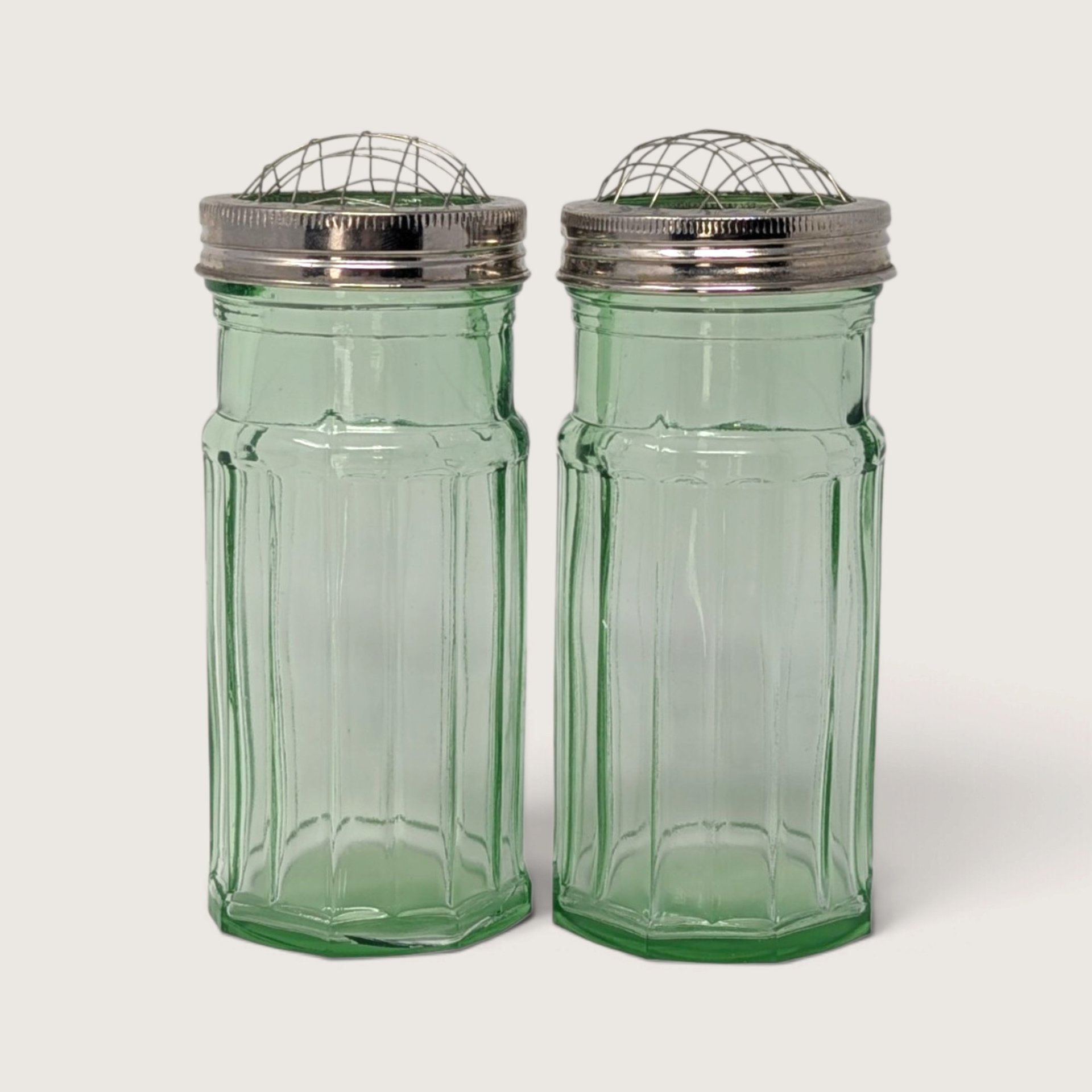 A pair of vintage green glass panel-cut vases featuring metal screw-on caps with domed wire flower frog inserts against a neutral background.