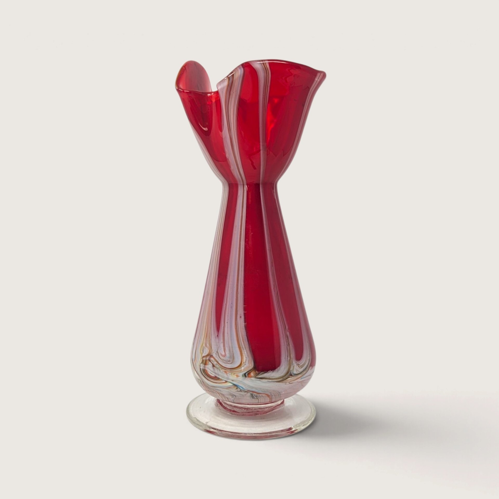 Vintage hand blown ruby red art glass bud vase with white pulled feather swirls and clear foot on white backdrop.   