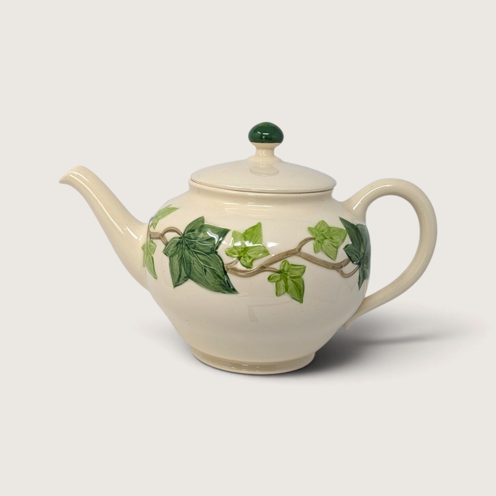 Vintage Franciscan Ivy ceramic teapot with embossed green ivy leaves and matching green lid finial on white background.   
