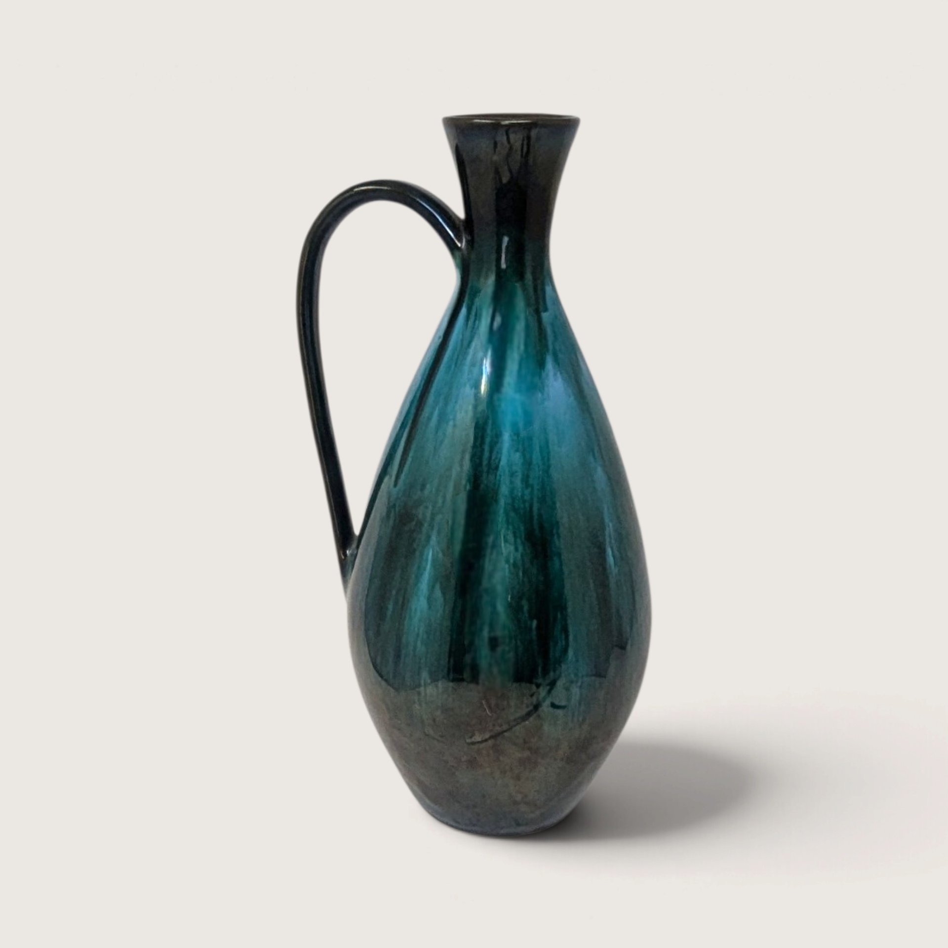 Vintage Blue Mountain Pottery tall ceramic teardrop pitcher vase with green and black flowing drip glaze on white backdrop.   