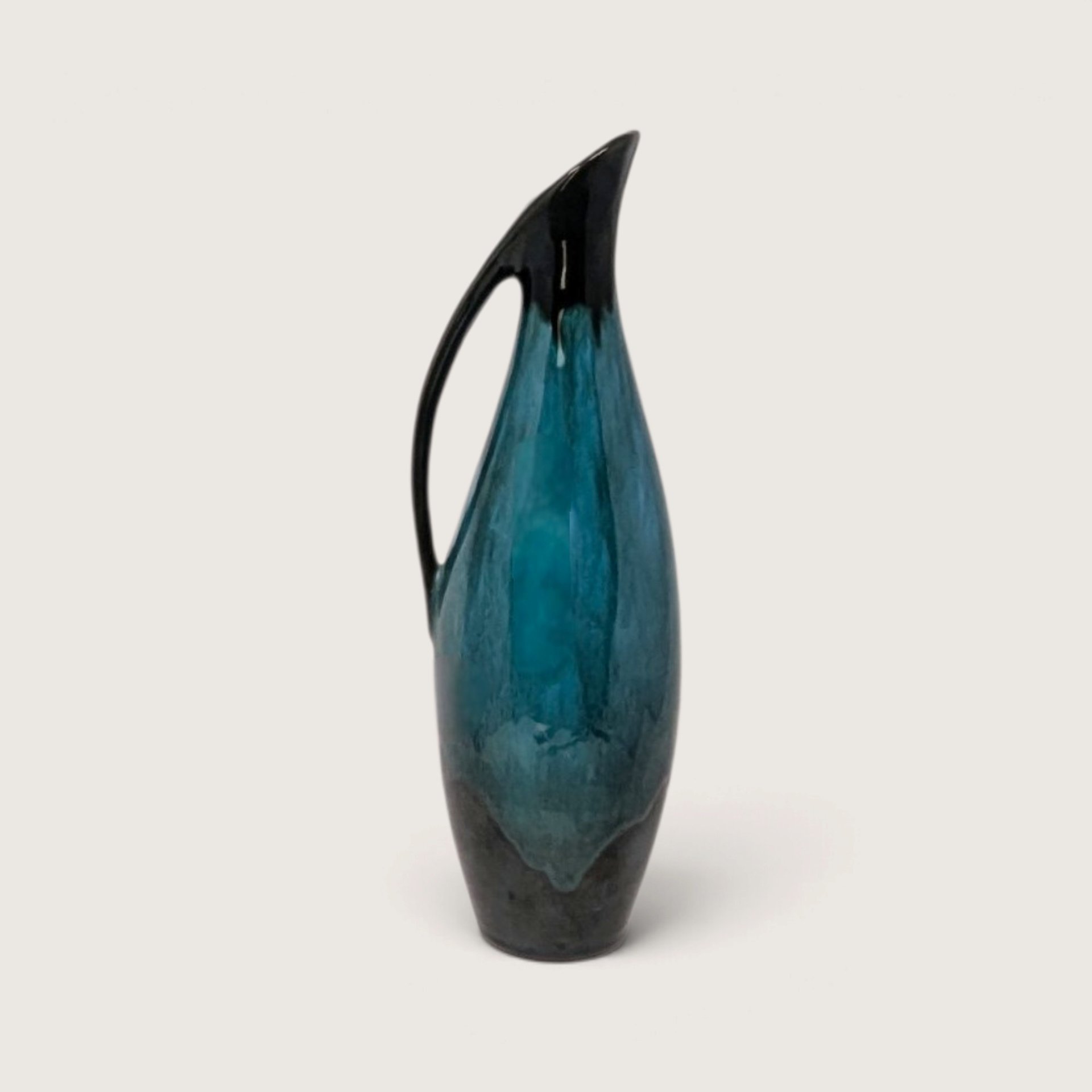Vintage Blue Mountain Pottery slender ceramic pitcher vase with flowing green and black drip glaze on white backdrop.   