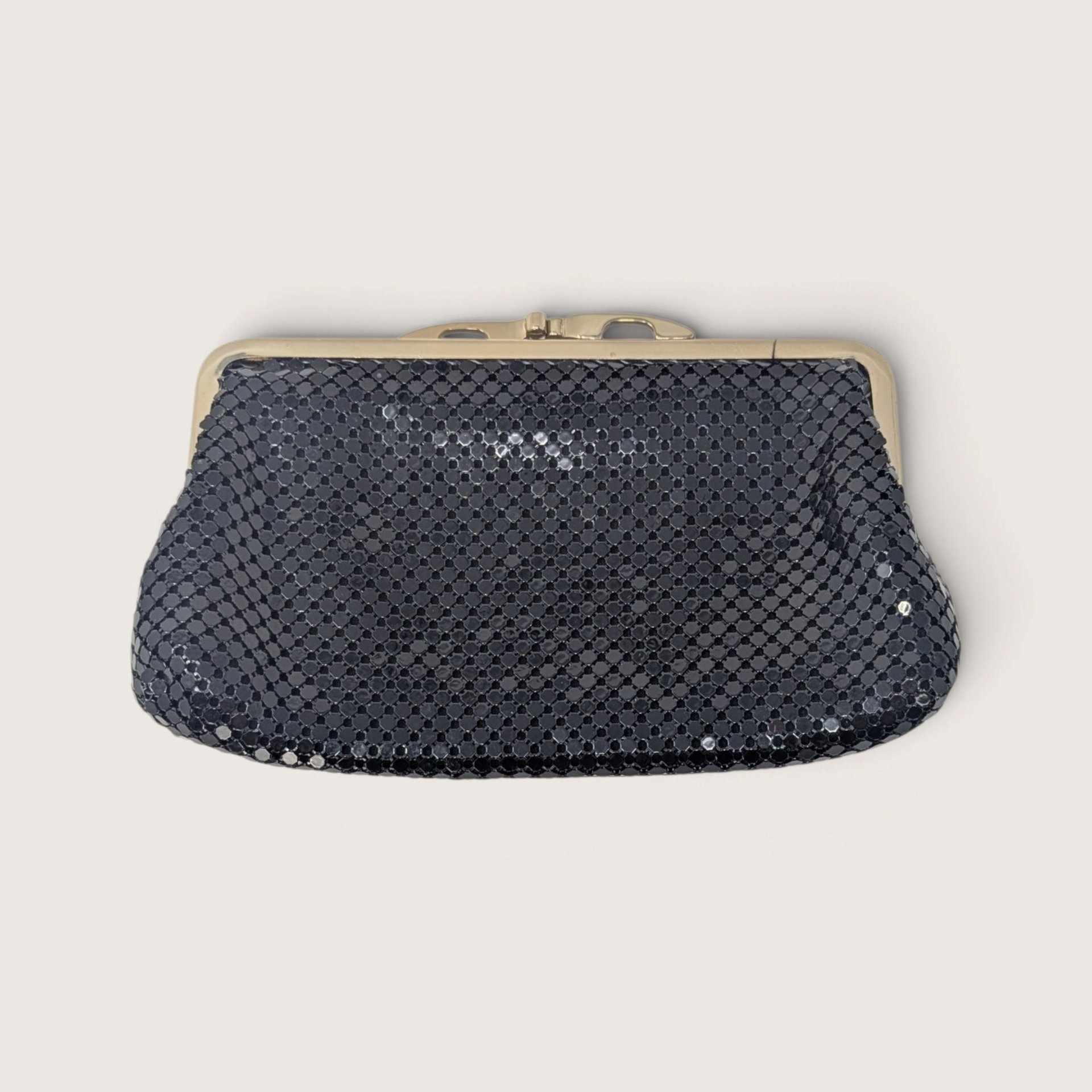 Vintage Whiting and Davis International black metal mesh evening clutch purse with gold-tone kiss lock on a light background.   
