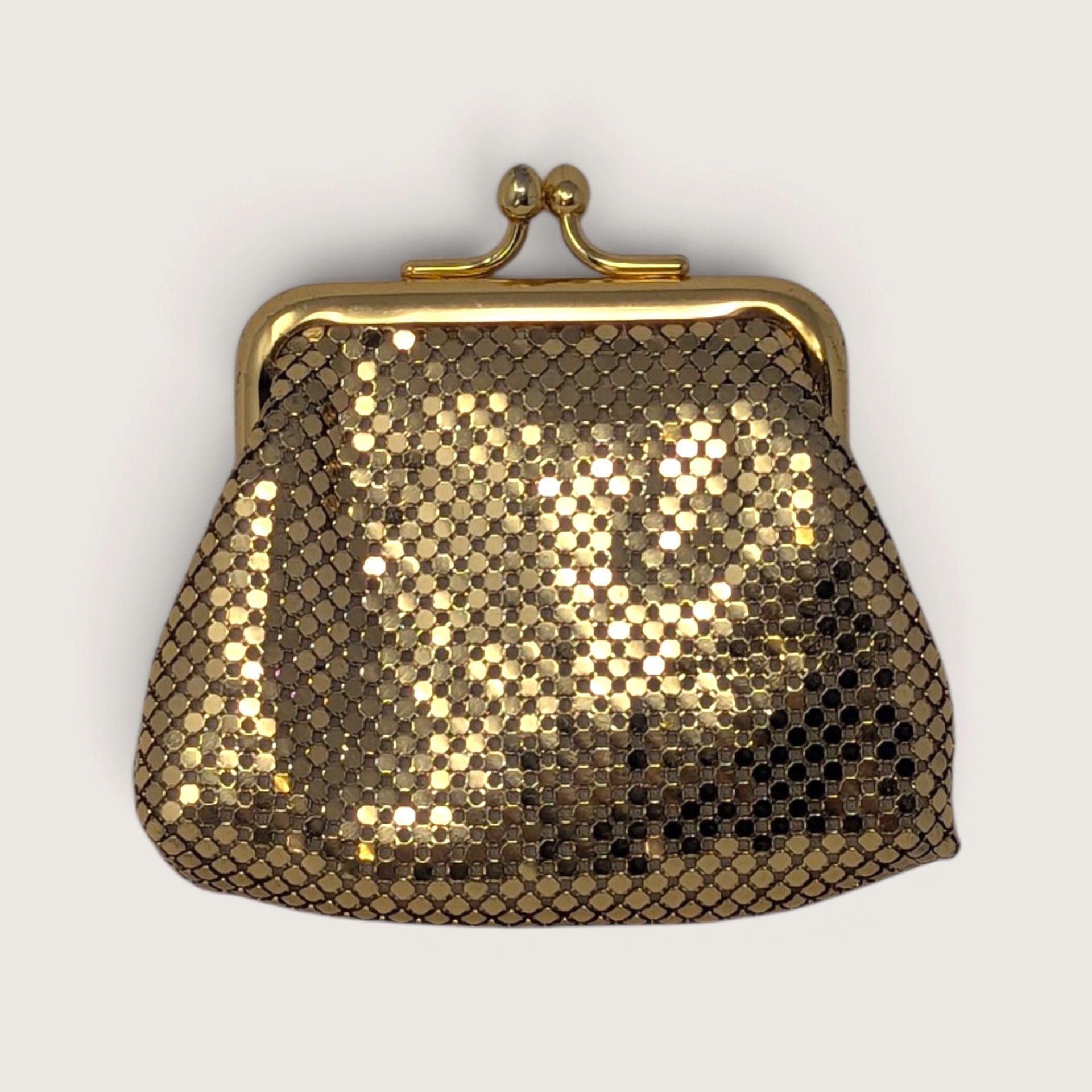 Vintage Whiting and Davis International gold metal mesh kiss lock coin purse wallet on a light background.   