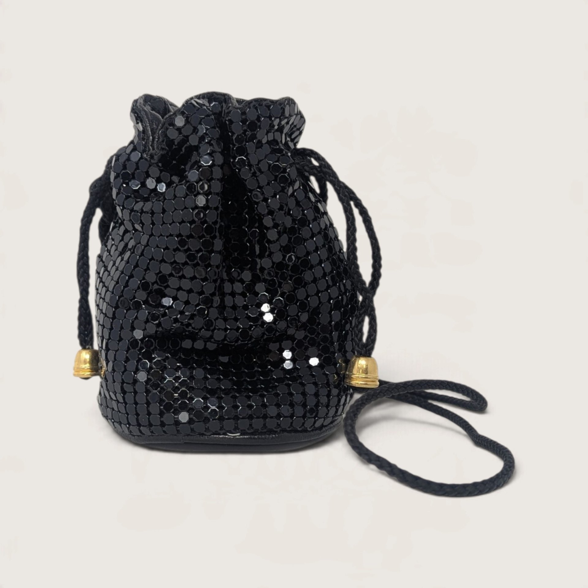 Vintage black enameled metal mesh mini drawstring bucket bag with gold bell cord ends on a light backdrop.   
