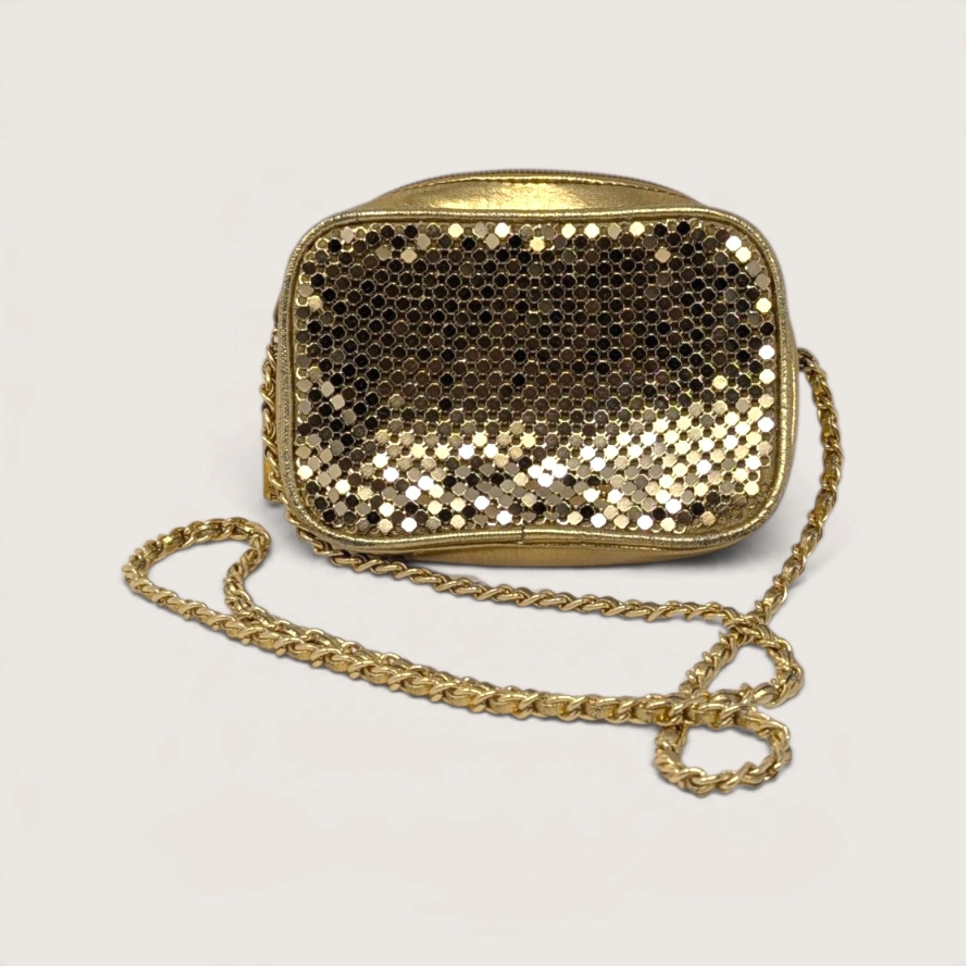 Vintage Whiting and Davis International gold metal mesh mini crossbody bag with curb chain strap on white backdrop.   
