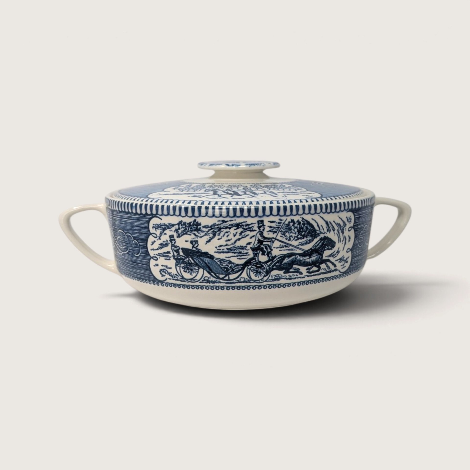 Vintage Royal China Currier and Ives blue transferware round covered casserole dish with carriage motif on a white background.   