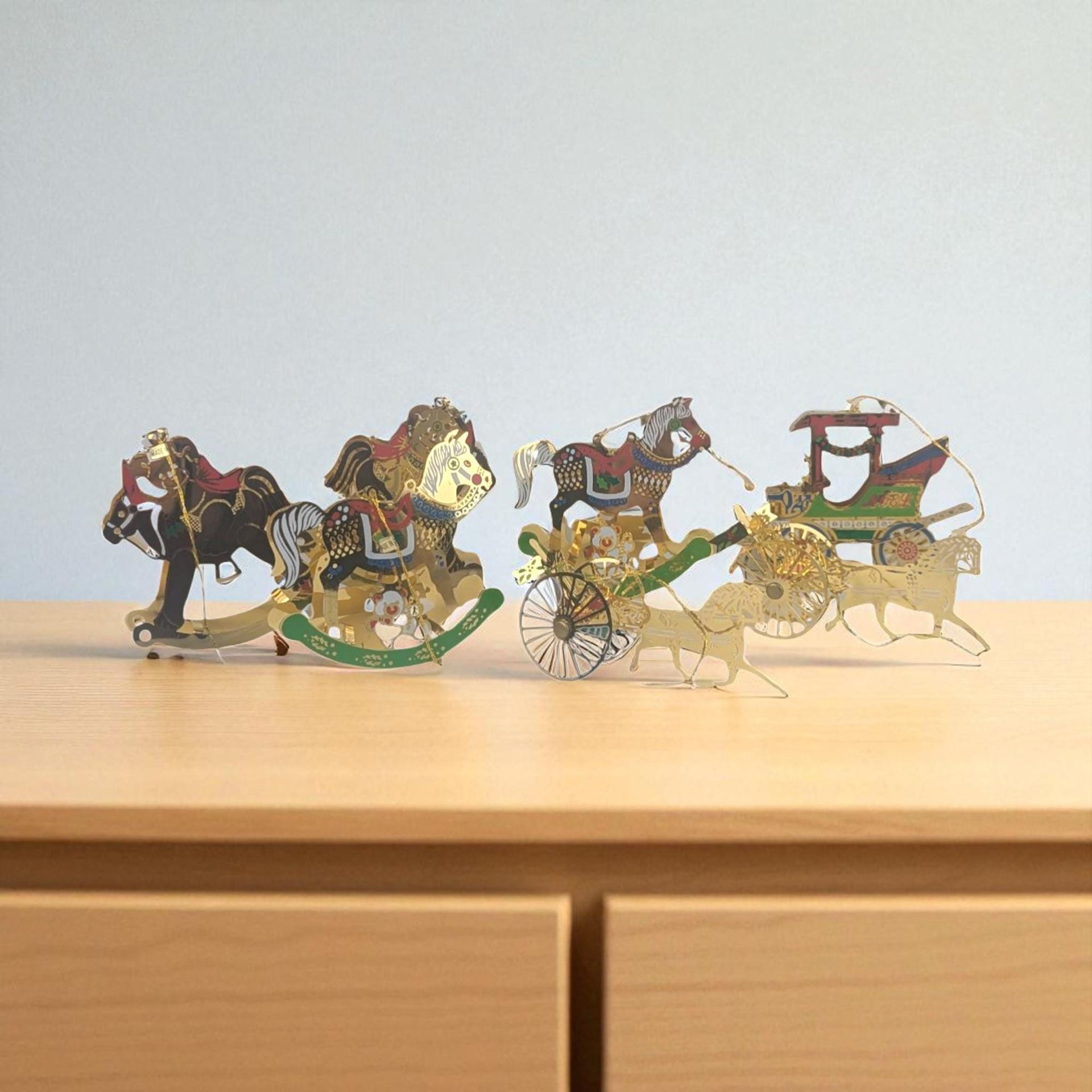A horizontal view of a set of seven vintage brass-colored metal Christmas ornaments. The collection features a variety of classic equestrian and holiday designs, including several intricate rocking horses, a detailed horse-drawn buggy with a carriage, and other ornate filigree shapes. Each piece has a warm, golden metallic finish with delicate cutout details.