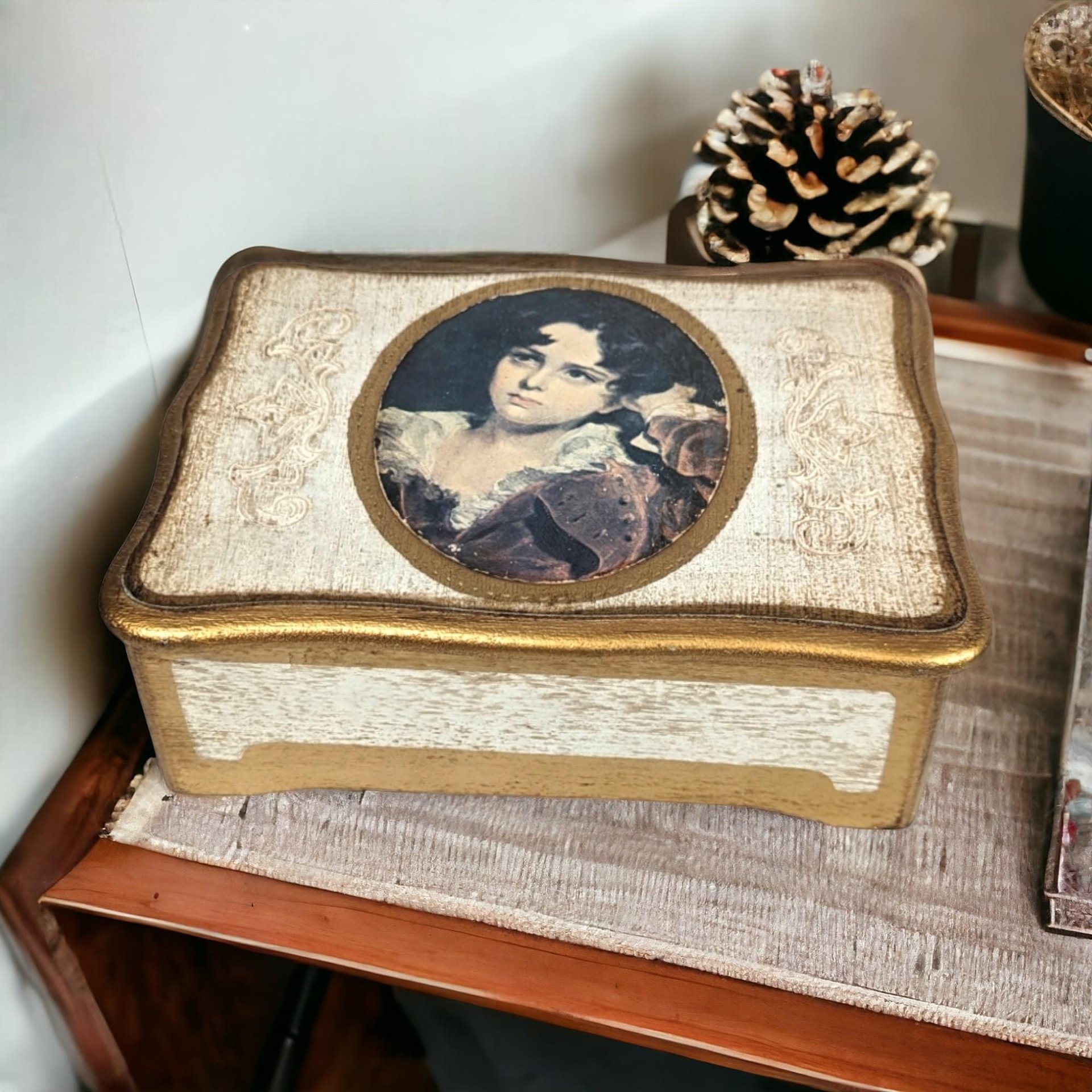 A white wooden jewelry music box with gold trim featuring a mid-century illustration of a young boy on the lid and a plush red velvet interior.