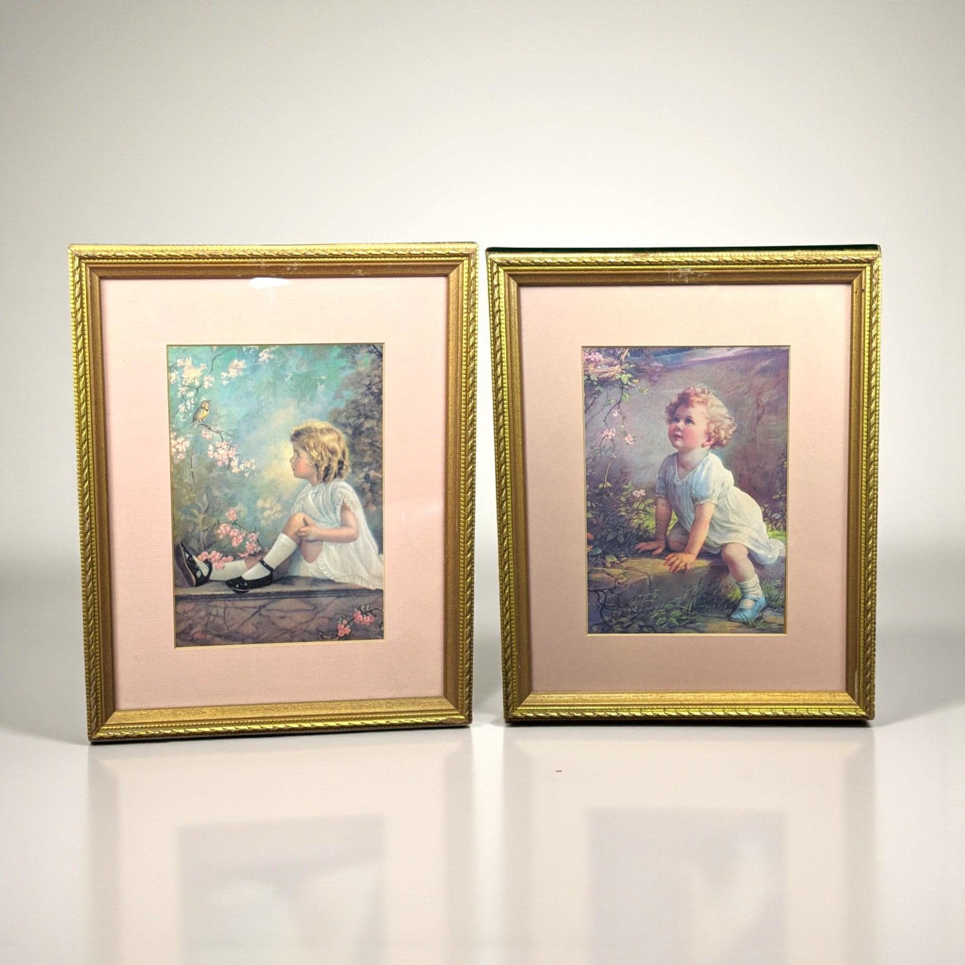 Two matching vintage wood frames containing portrait prints of little girls. One print, "Song of the Bluebird" by Zula Kenyon, shows a girl in a soft dress looking upward at a bird. The second, "Song of the Lark" by Florence Lindsey, features a similar ethereal portrait. The frames have a dark, aged finish with ornate period detailing.