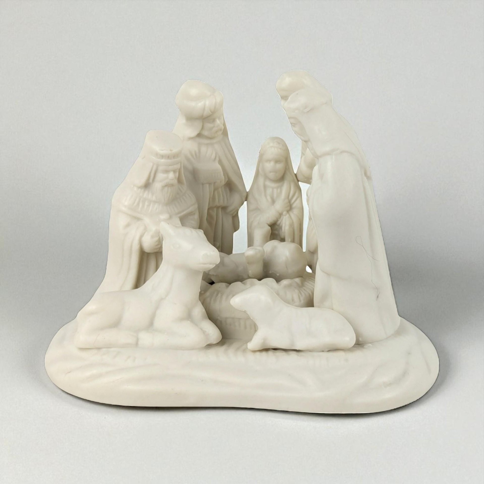 A monochromatic white porcelain nativity scene featuring a smooth, matte texture. The sculpture depicts a group of figures and animals on a rounded base, including the Holy Family and Wise Men, characterized by soft silhouettes and refined, uniform coloring.