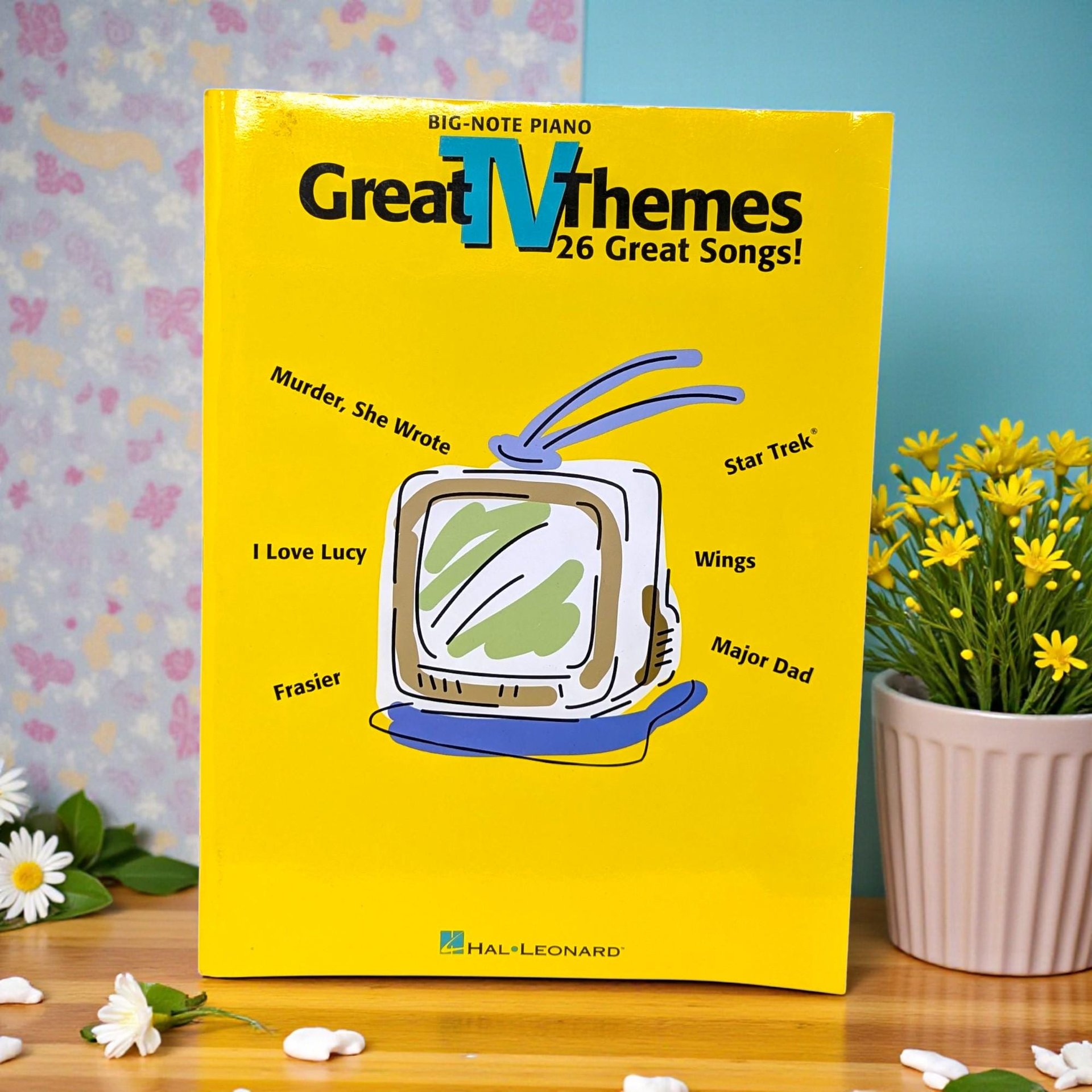 A large format softcover music book with a black cover featuring a montage of classic television screens. The typography is bold and colorful, showcasing a collection of famous small-screen melodies in a clean, preserved silhouette.