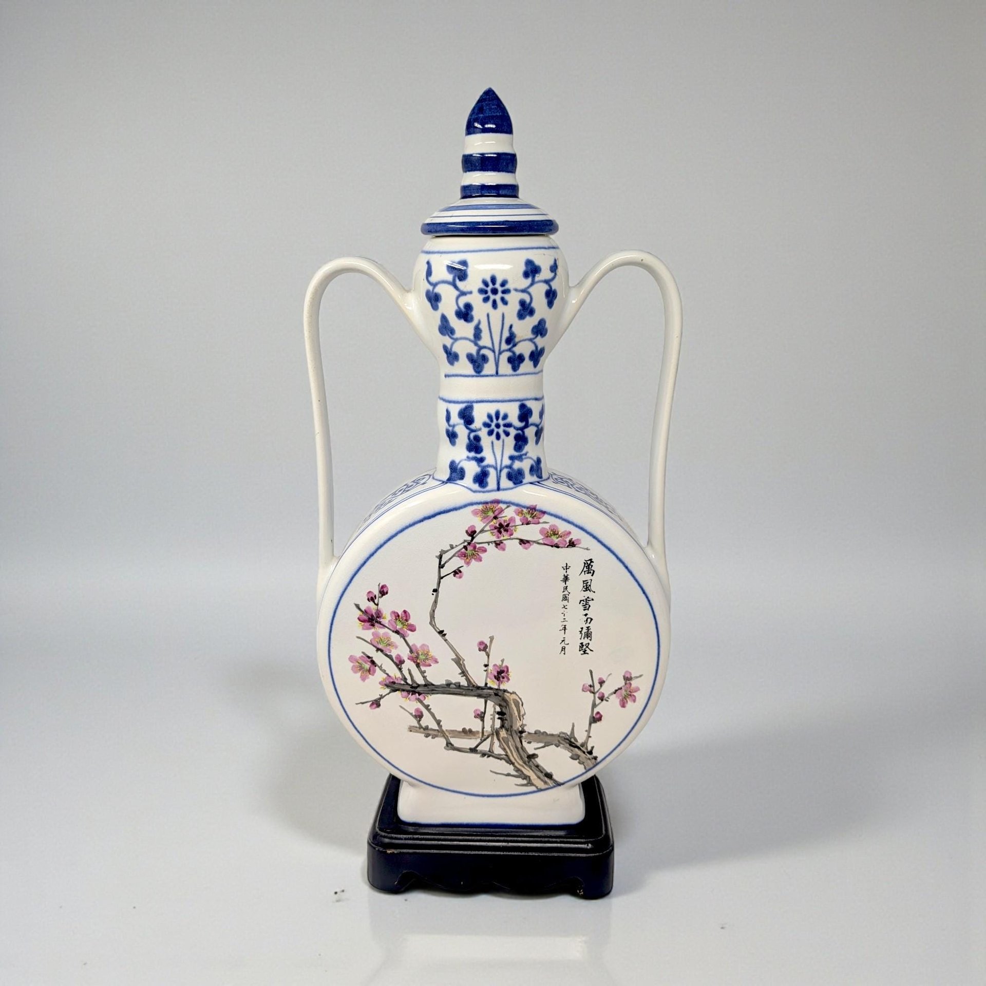 A large, circular porcelain moon flask with a slender neck and two small handles. The face features a detailed blue and white transfer of a blooming lotus and rose, set against a stark white glaze.