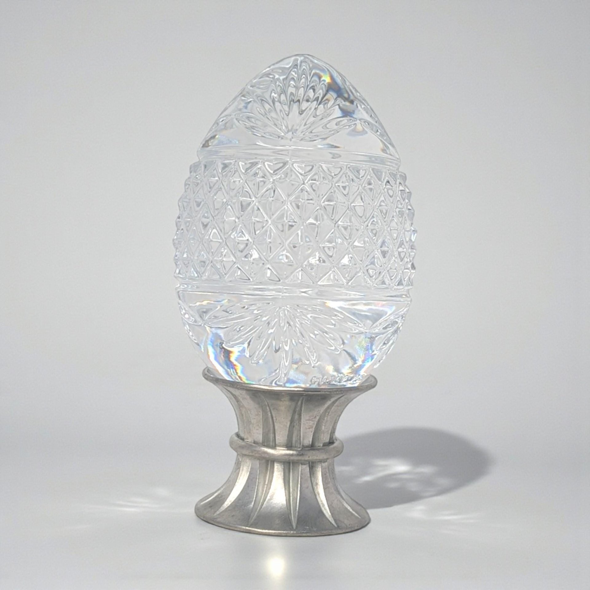 A clear 24% lead crystal egg with a deep diamond-cut waffle pattern, resting on a polished silver-toned pewter stand.