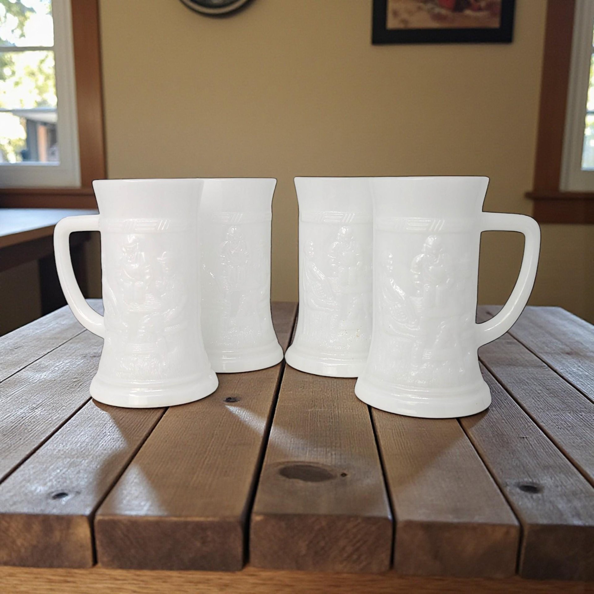 A set of four white milk glass beer mugs with a raised relief tavern scene. Each mug features a detailed embossed pattern of a German-style pub with figures and a sturdy handle against a glossy white background.