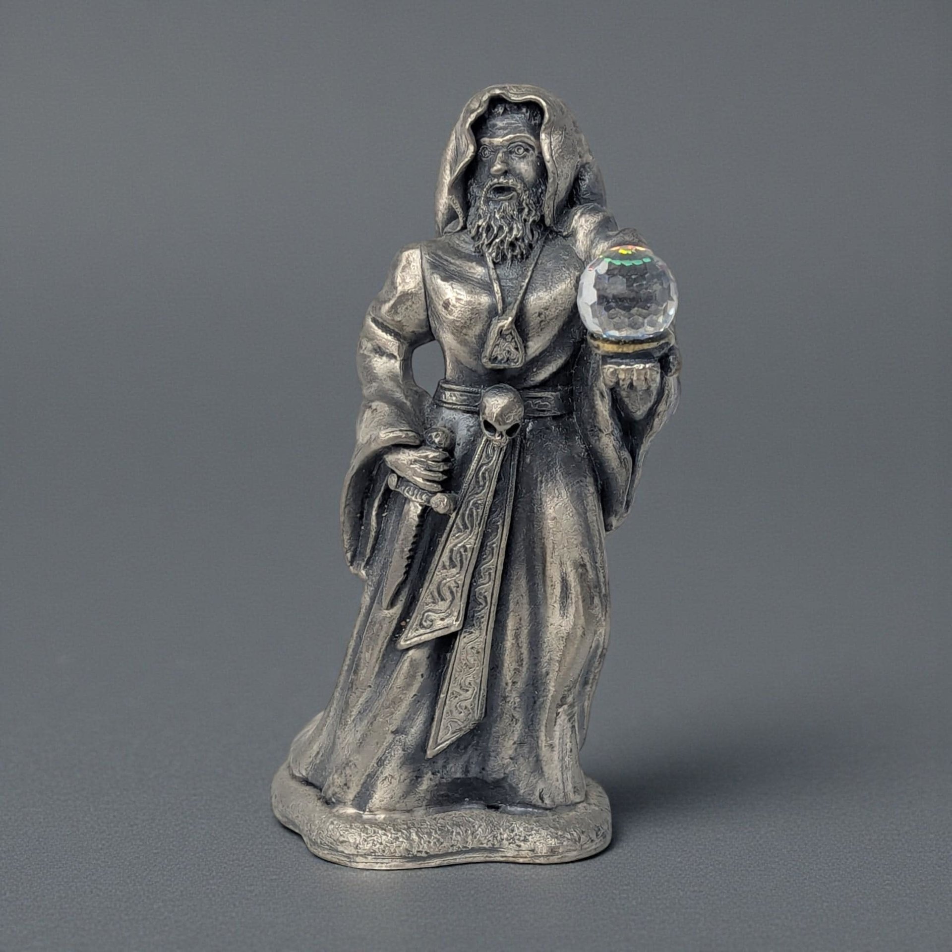 A tall pewter sorcerer figure wearing a long hooded robe and holding a staff. A large translucent crystal orb is embedded in the base. The metal has a dark antiqued finish with a vertical, powerful silhouette.