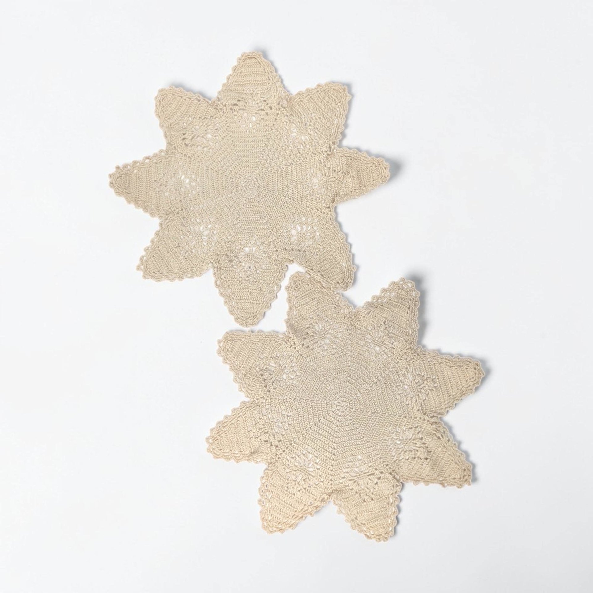 Two ivory-colored hand-crocheted doilies in an eight-point star silhouette. Intricate openwork lace with concentric geometric patterns and a picot edge. Subtle age-related cream patina across the thread.