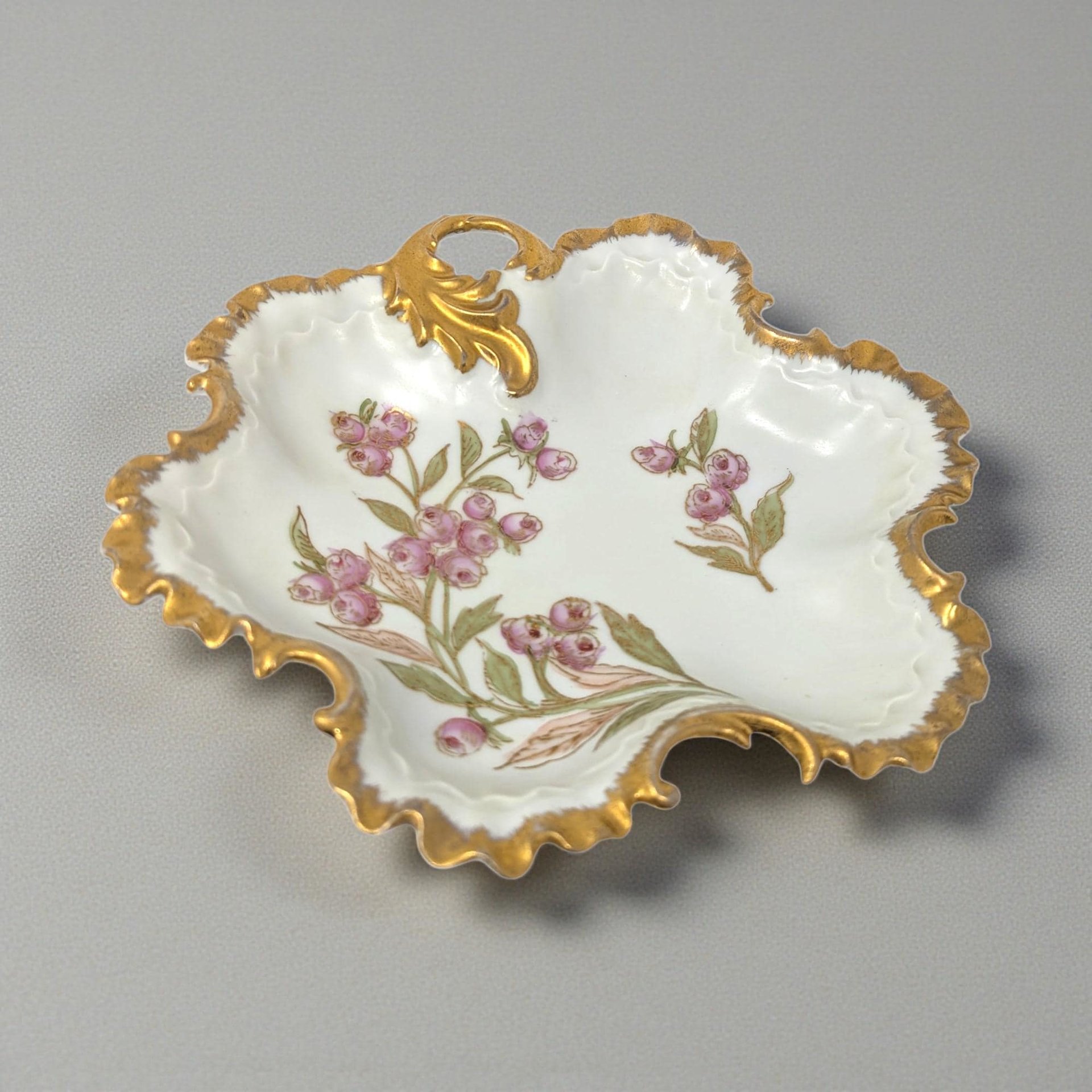 A square-shaped porcelain serving dish with rounded corners and two integrated handles. The center features a delicate spray of pink flowers and green leaves, finished with a bright gold scalloped rim on a crisp white background.
