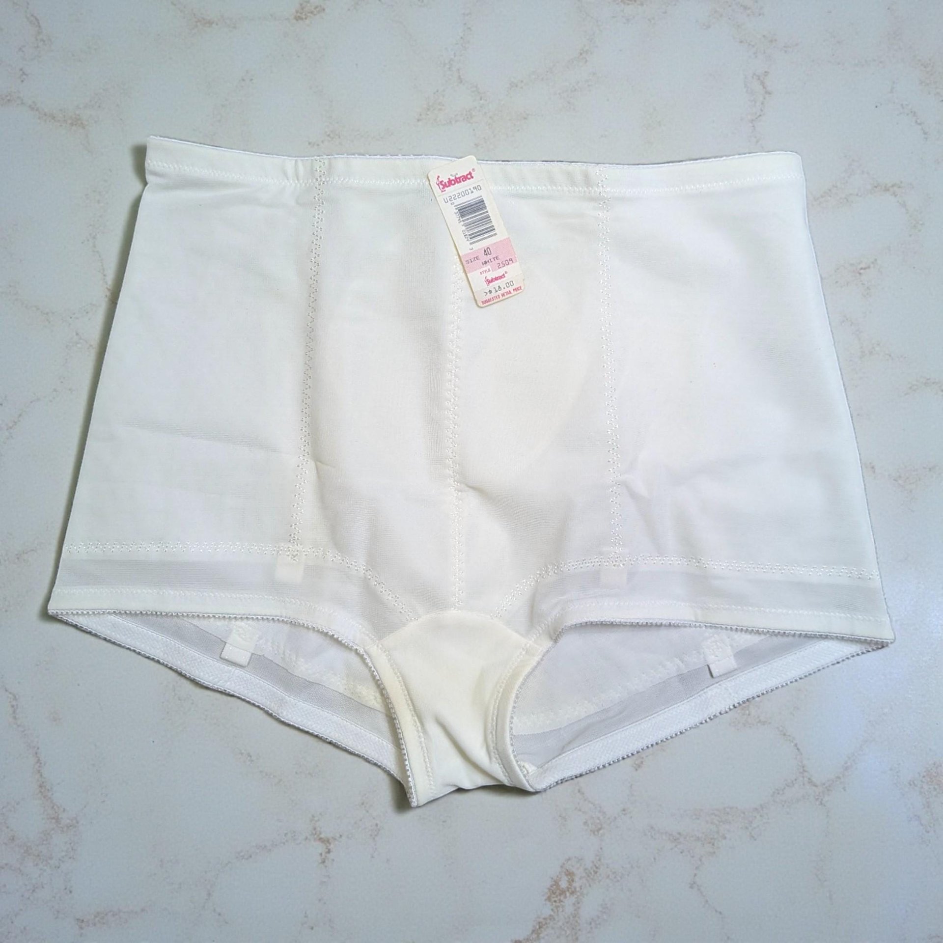 A pair of vintage white high-waisted control briefs with a textured floral pattern on the front panel. The original paper tag is still attached to the waistband.