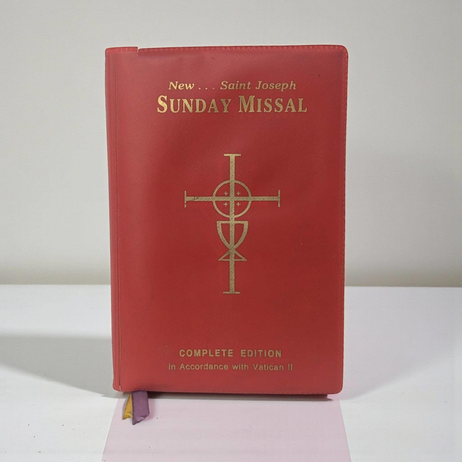 A thick, pocket-sized softcover book with a flexible white cover featuring a golden religious emblem. The spine is substantial, and the thin cream-colored pages show a slight natural rippling from age.