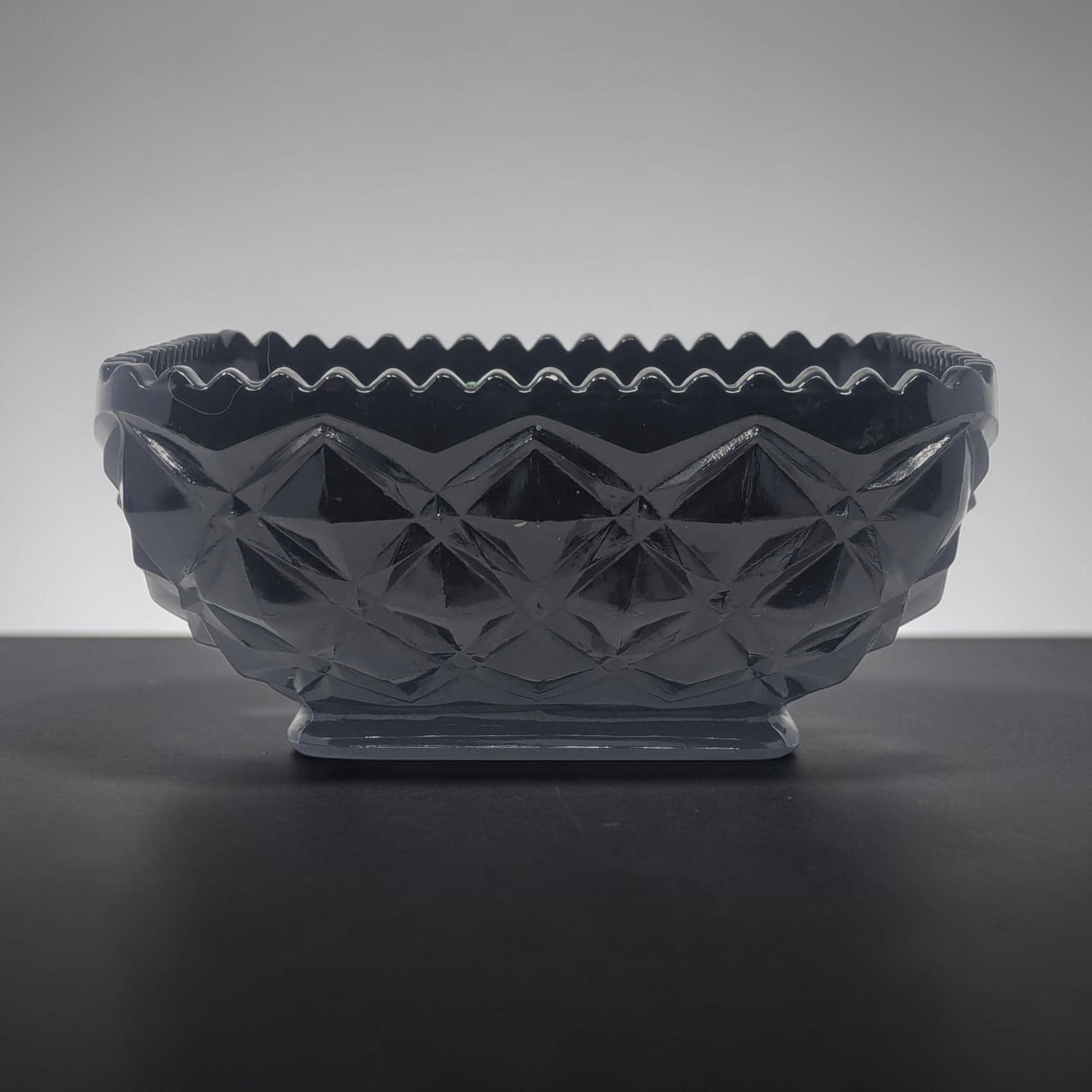 Deep black opaque glass bowl with a relief diamond block pattern across the exterior. Scalloped serrated rim and a rectangular pedestal base. High-gloss finish reflecting light off geometric facets.